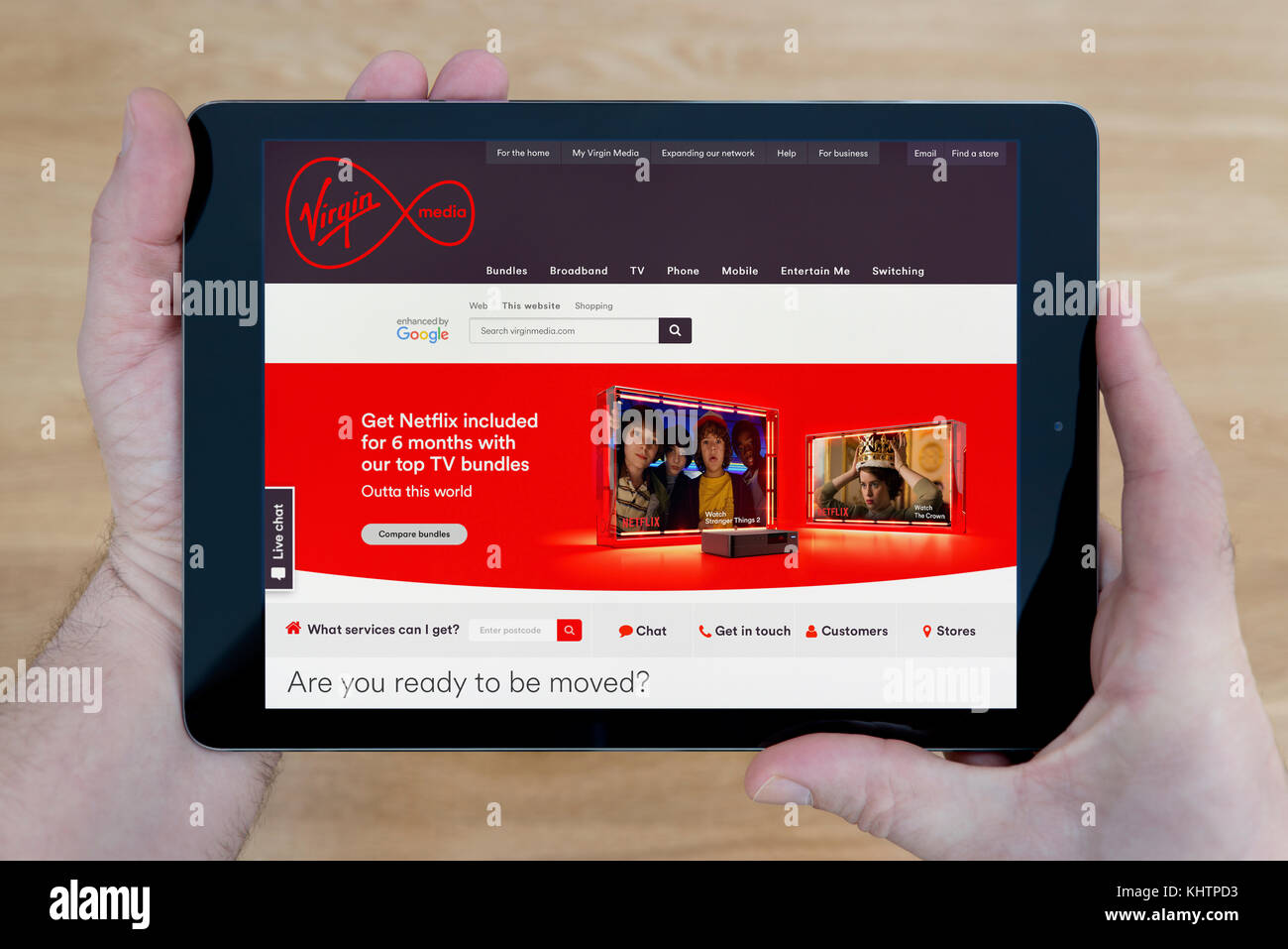 Ein Mann schaut auf die Virgin Media Website auf seinem iPad tablet device, Schuß gegen einen hölzernen Tisch top Hintergrund (nur redaktionelle Nutzung) Stockfoto