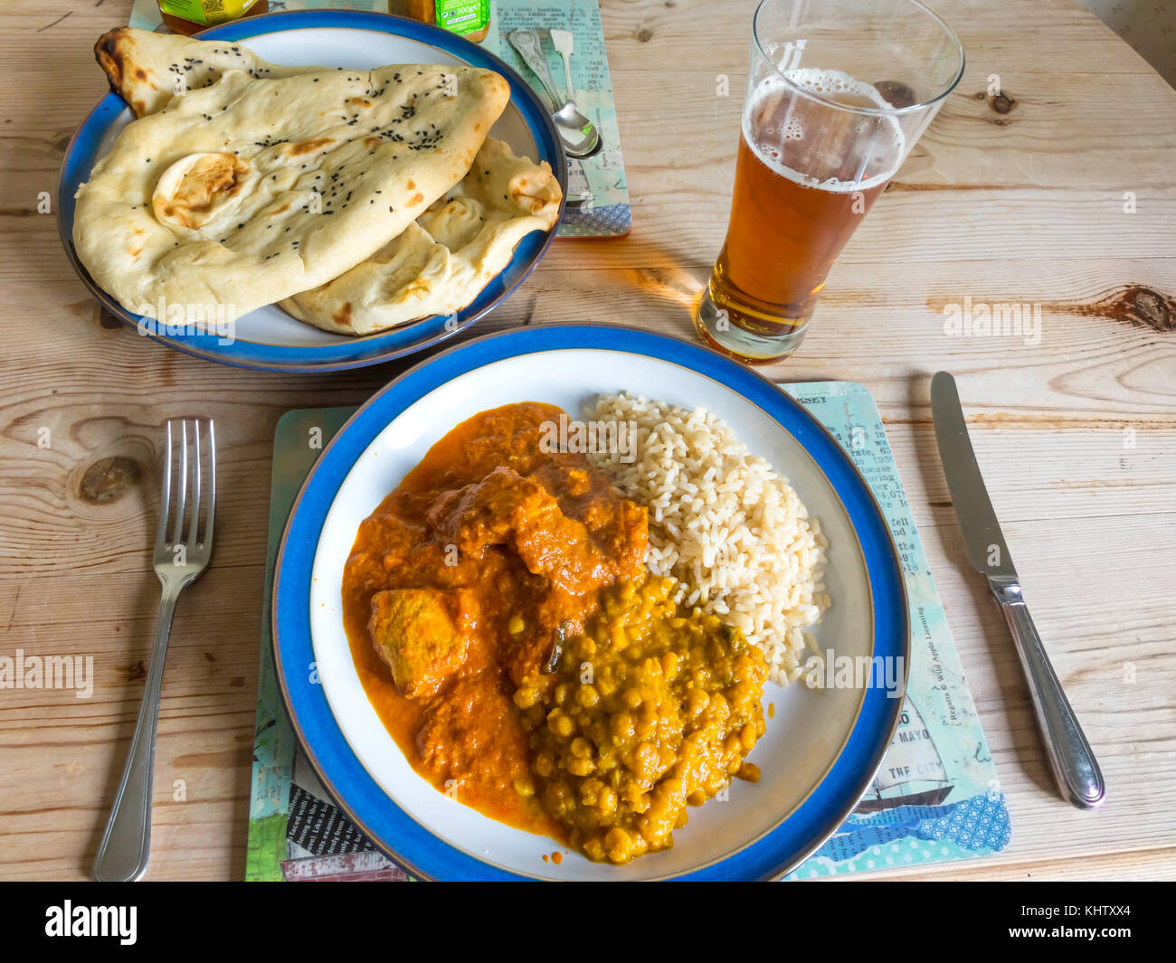 Indische Speisen zum Mitnehmen serviert zu Hause Chicken Madras Curry, Tarka Dahl, Tandoori Naan, Basmati Reis, Mango und Limette Chutneys und ein Glas IPA Stockfoto