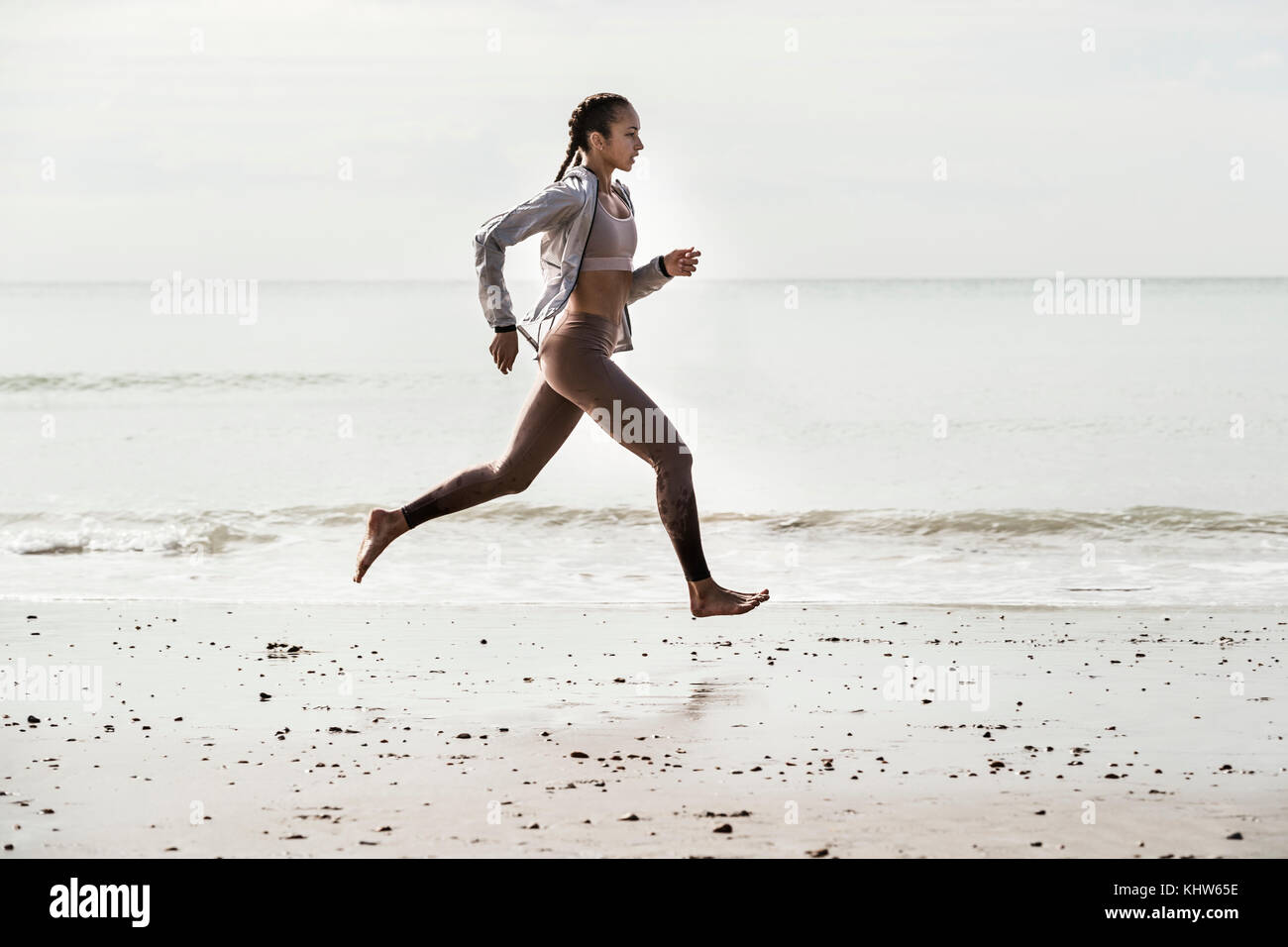 Seitenansicht des jungen weiblichen Läufer laufen barfuß entlang der Wasserkante am Strand Stockfoto