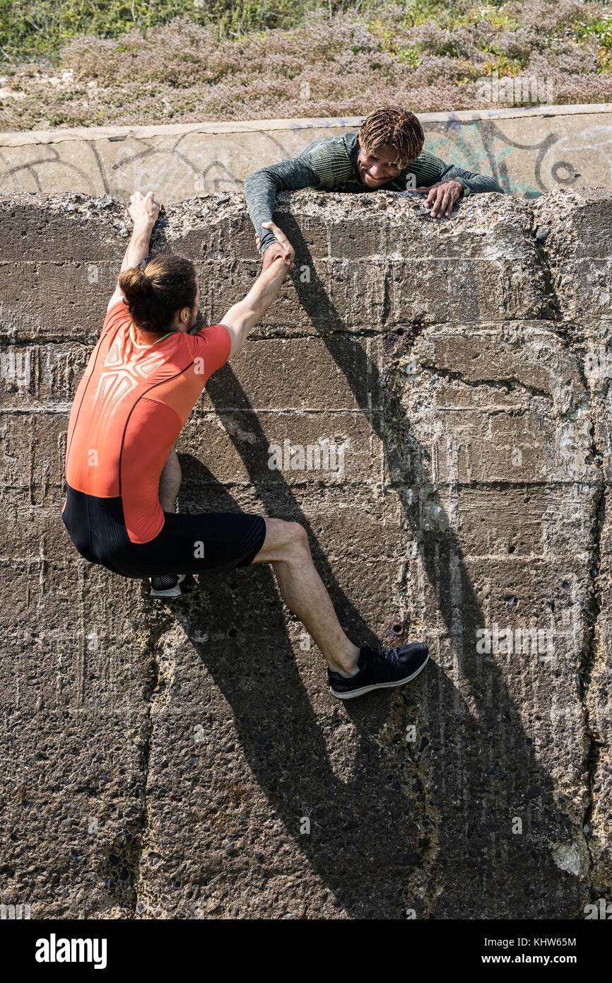 Junge männliche freien Kletterer an der Oberseite des Sea Wall helfen Freund Aufstieg Stockfoto