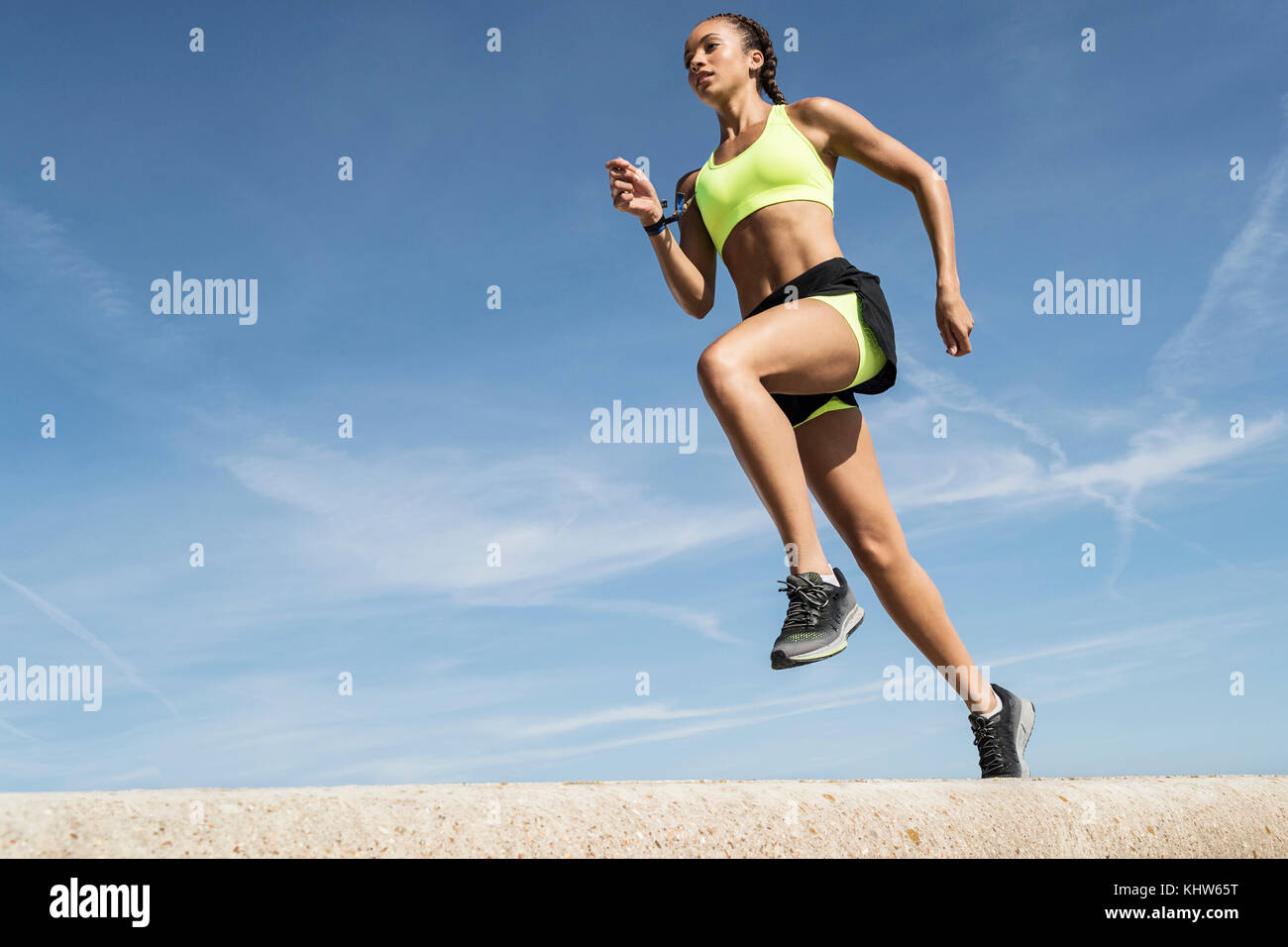 Low Angle View der jungen Läuferin entlang Sea Wall gegen den blauen Himmel läuft Stockfoto