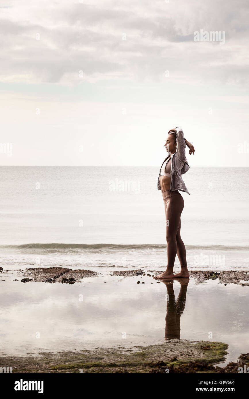 Junge weibliche Läufer an Water's Edge am Strand stretching Arms Stockfoto