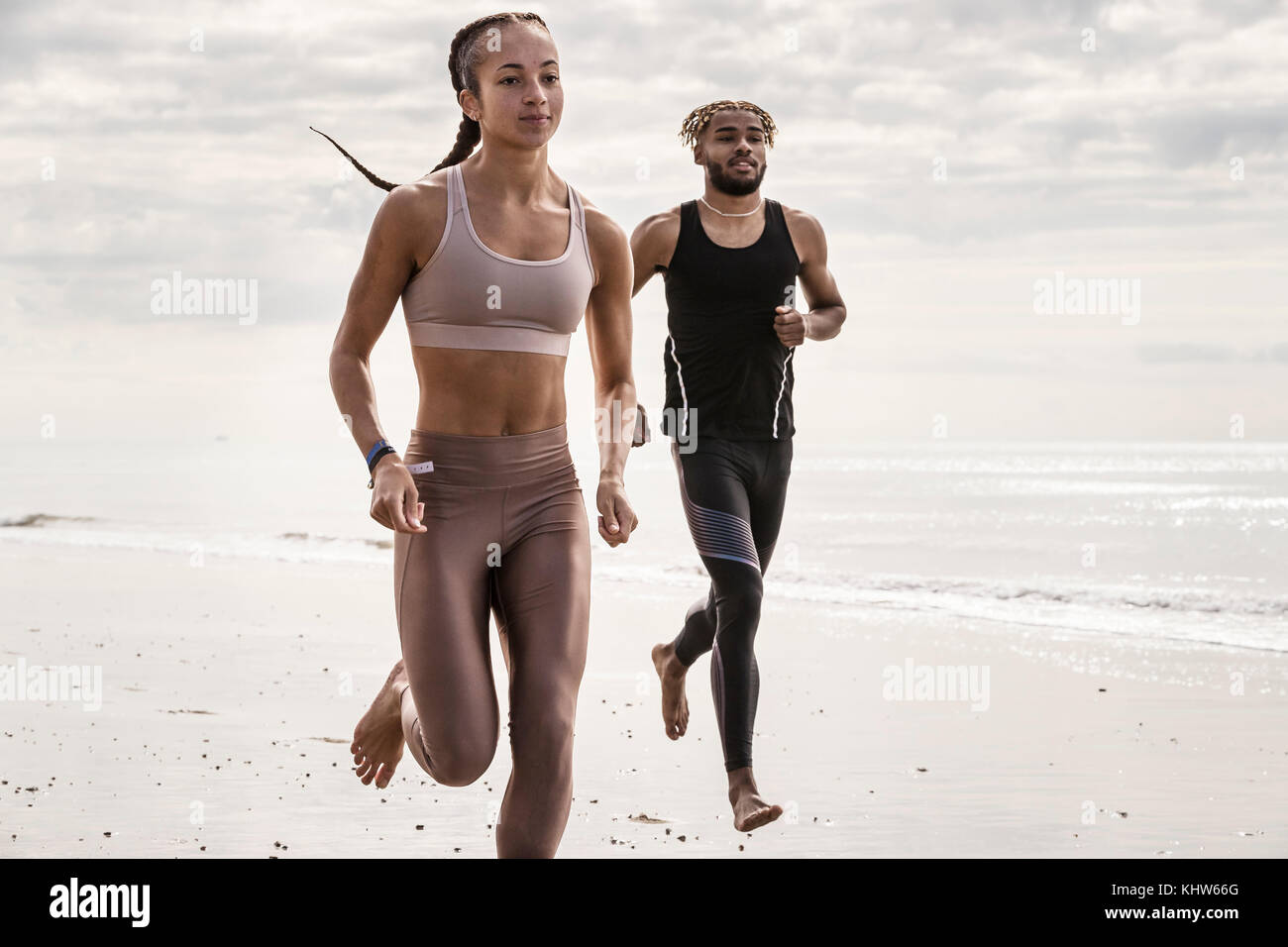 Junge männliche und weibliche Läufer laufen barfuß am Strand Stockfoto