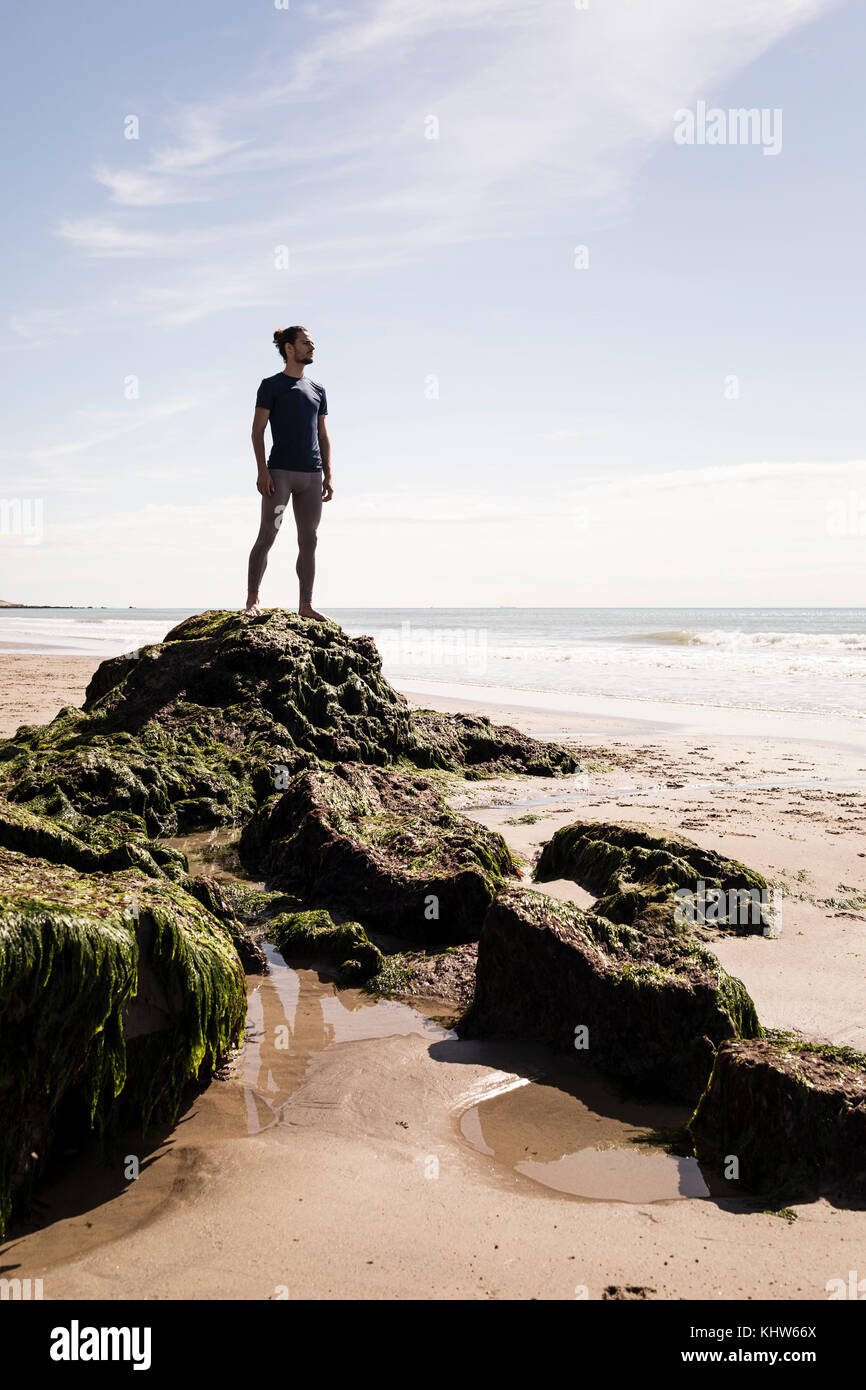 Junge männliche Läufer mit Blick auf das Meer vom Strand rock Stockfoto