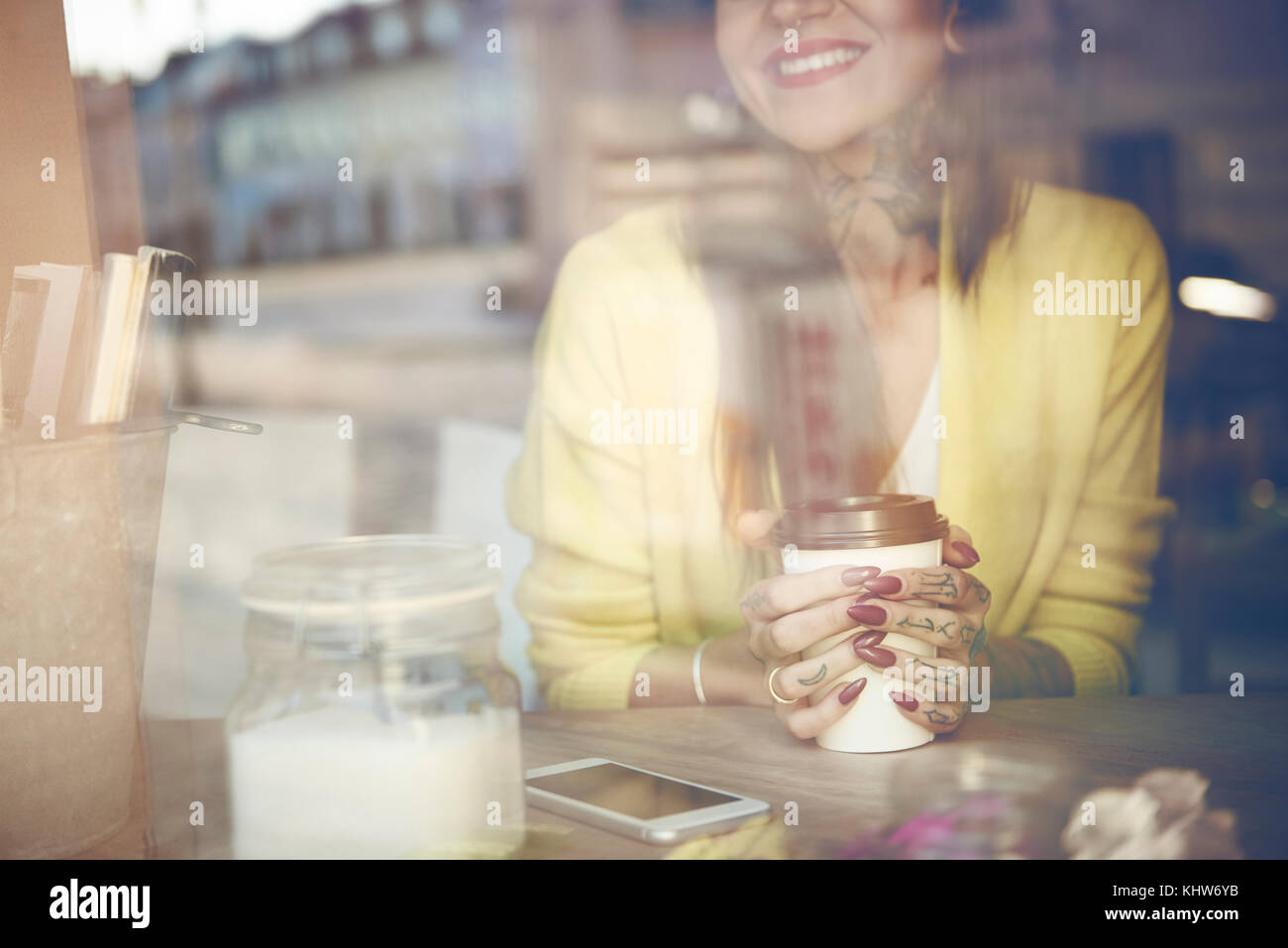 Junge Frau im Cafe sitzen, Kaffee Tasse, Tätowierungen, Blick durch Fenster Cafe, mittlere Partie Stockfoto