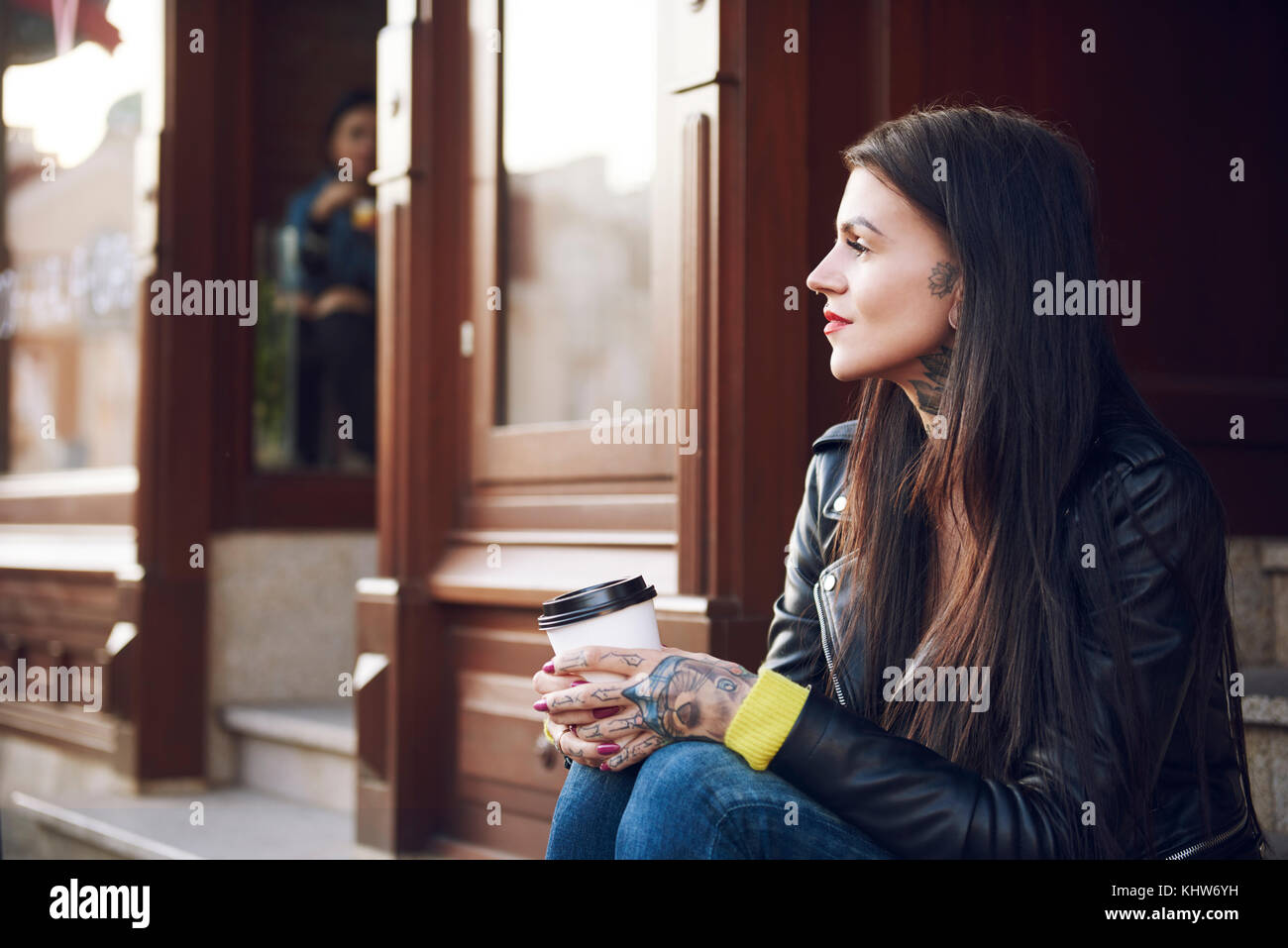 Junge Frau sitzt im Freien, Kaffeetasse, Tattoos auf Händen Stockfoto