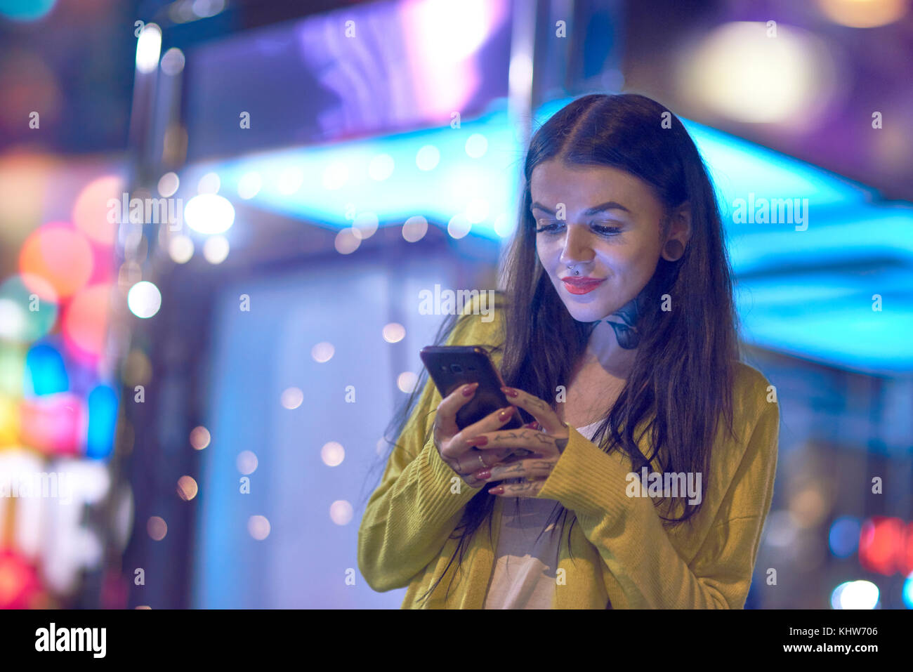 Junge Frau draußen in der Nacht, mit Smartphone, Tattoos auf Hals und Händen Stockfoto