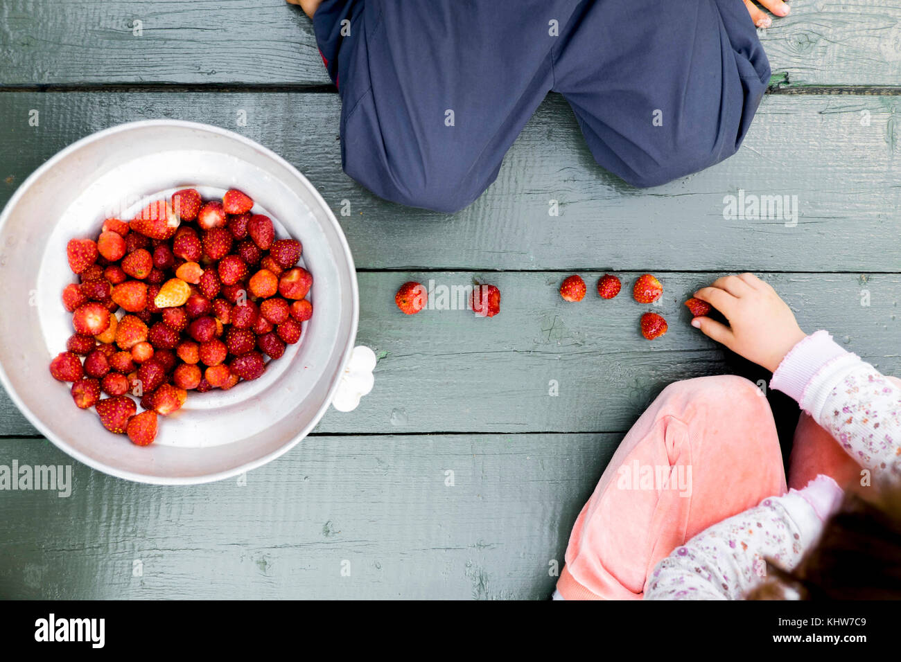 Zwei Kinder sitzen auf Holzboden, Schüssel mit Erdbeeren neben Ihnen, Ansicht von oben Stockfoto