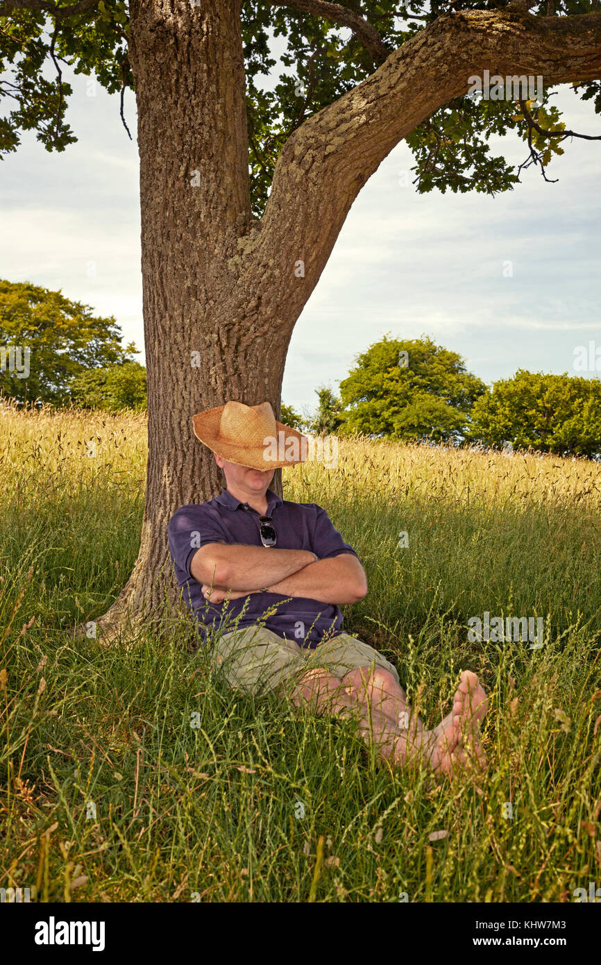 Ein Mann, ein Nickerchen im Schatten eines alten Baumes an einem heißen sonnigen Sommertag. Stockfoto