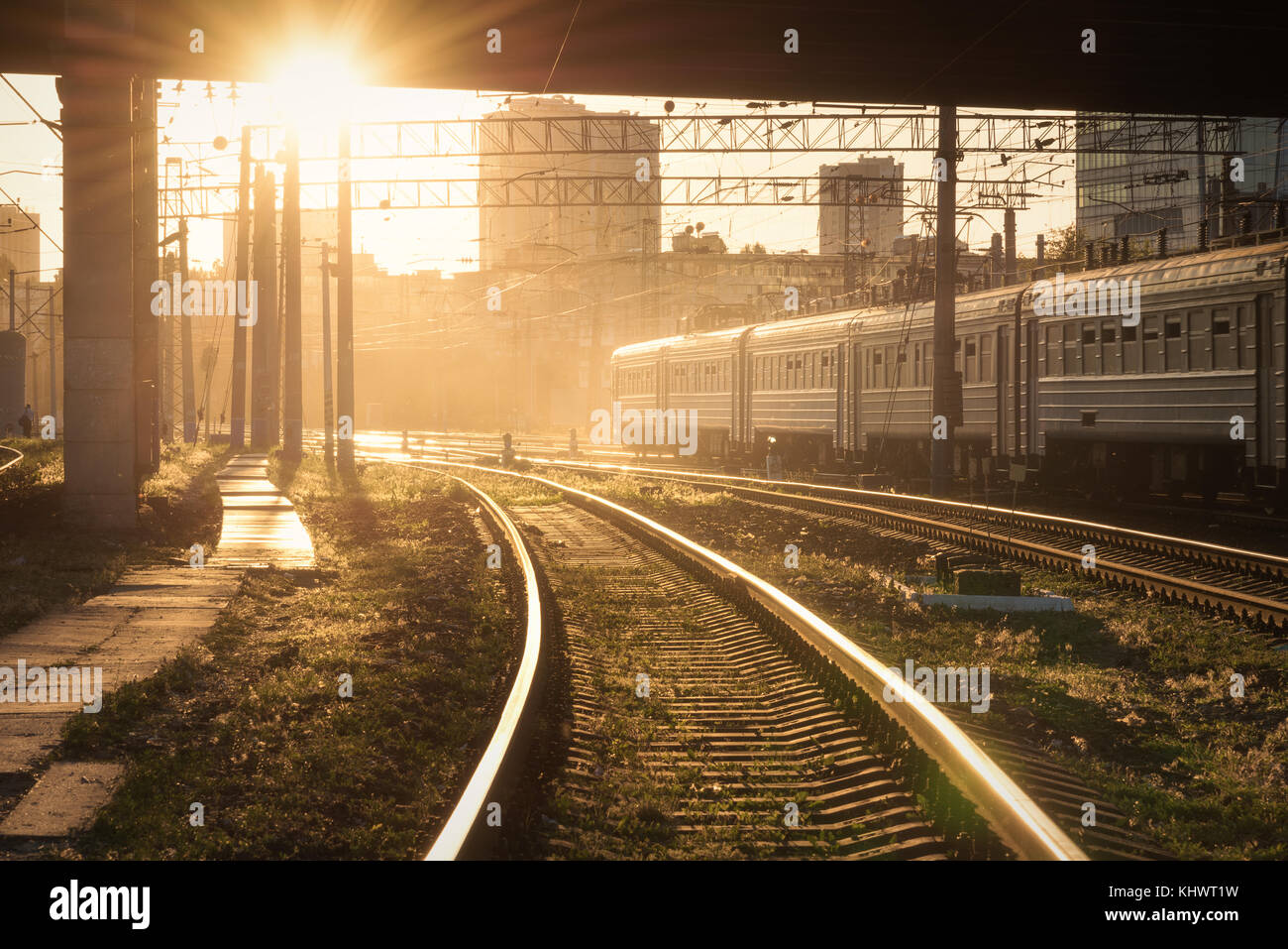 Schöne Aussicht mit Ampel, Eisenbahn- und fahrenden Zug bei Sonnenuntergang. Bahnhof. Bunte industrielle Landschaft mit Bahnsteig, Semaphor Stockfoto