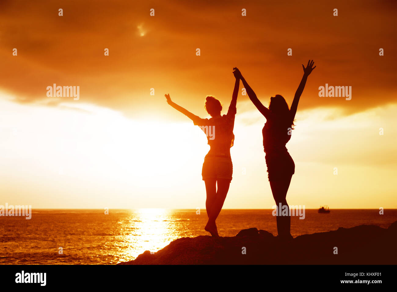 Zwei glückliche Mädchen mit erhobenen Armen auf dem Hintergrund des Sonnenuntergangs Stockfoto