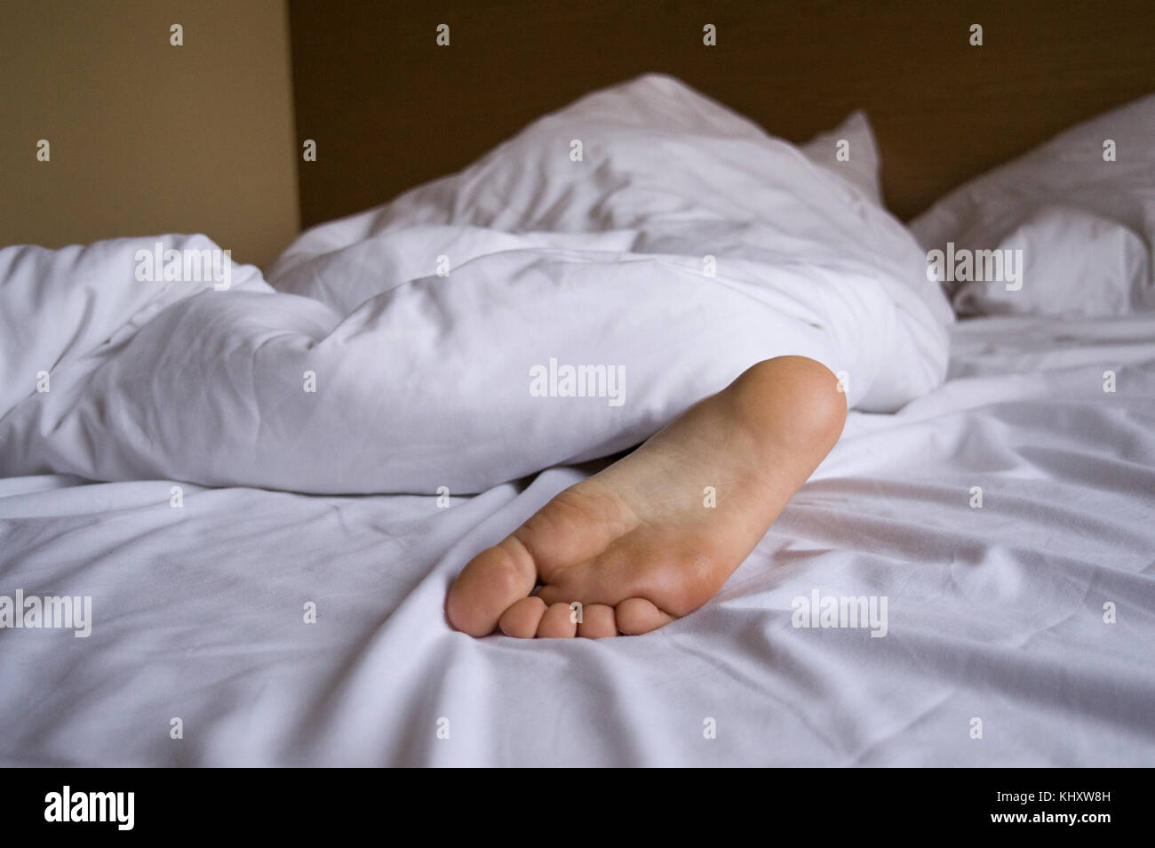 Ein Fuß einer schlafenden Person Frau oder Mann unter einer weißen Decke  auf dem Bett stecken Stockfotografie - Alamy