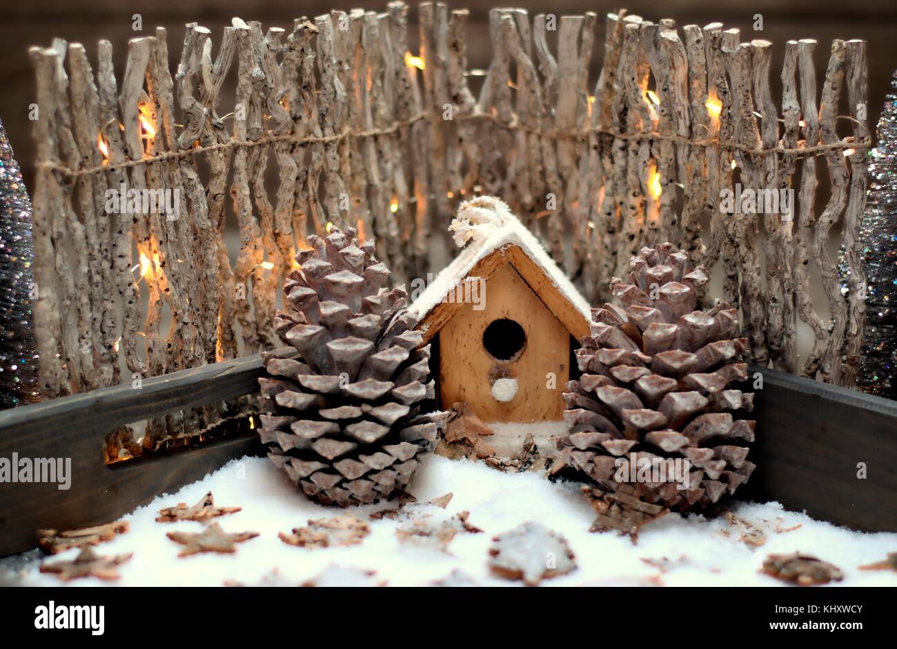 Weihnachtsdekoration, Feiertage und Dekor Konzept-Nahaufnahme Vogelhaus, Zapfen und Zaun mit Glühbirnen auf Schnee Hintergrund. Stockfoto