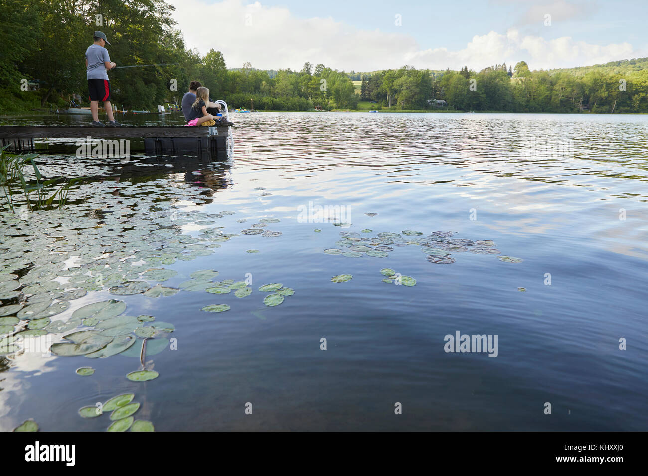 Drei Kinder auf Steg am See, jungen Fischen mit Angelrute Stockfoto