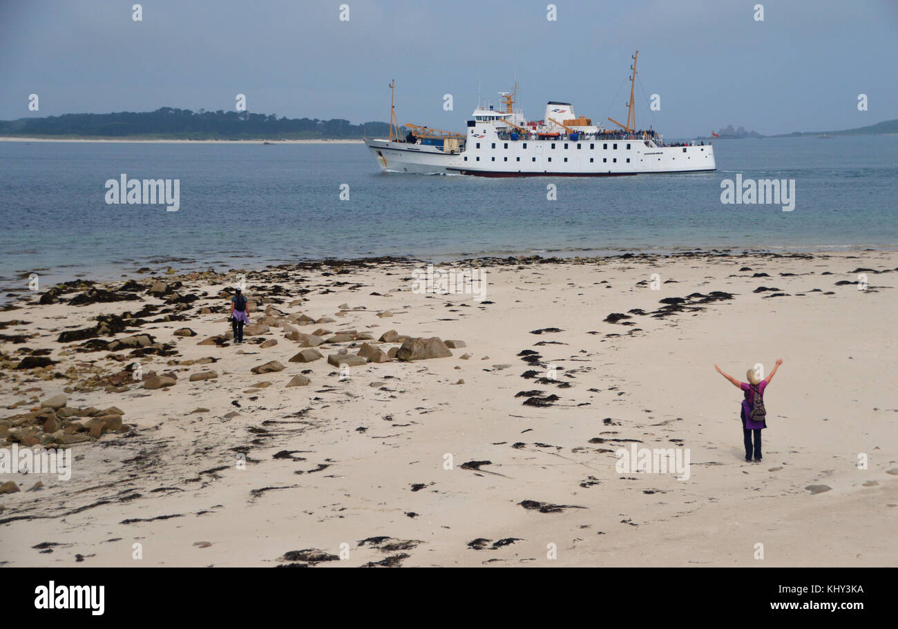 Frau winken auf bar Point Beach als rmv scillonian iii Fähre geht En-route von Penzance zu St Mary's, Isles of Scilly, Cornwall, UK. Stockfoto