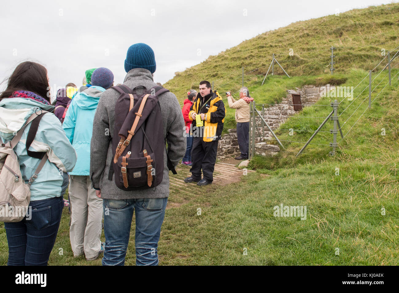 Der Reiseleiter spricht mit der Touristengruppe am Eingang zum neolithischen Kammerkairn Maeshowe, Teil des neolithischen Orkney-Weltkulturerbes Stockfoto