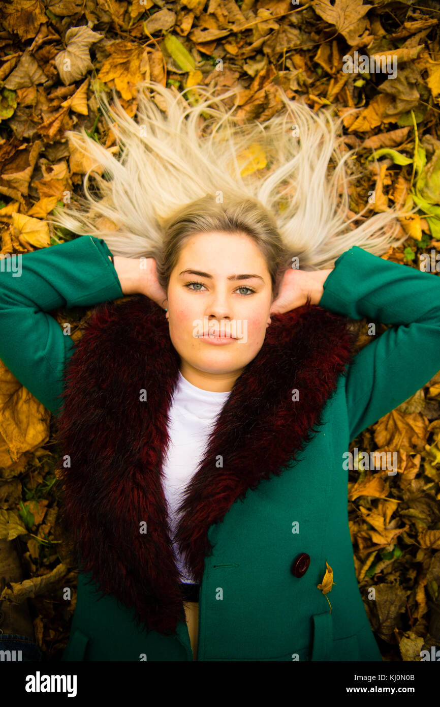 Jugendmädchen Modellierung in Großbritannien: Eine junge 16 jährige Pubertierende, trug einen Pelzbesatz grünen Mantel, der lag auf dem Rücken, die in den Blättern, modeling Posing im Freien an einem Herbsttag, Großbritannien Stockfoto