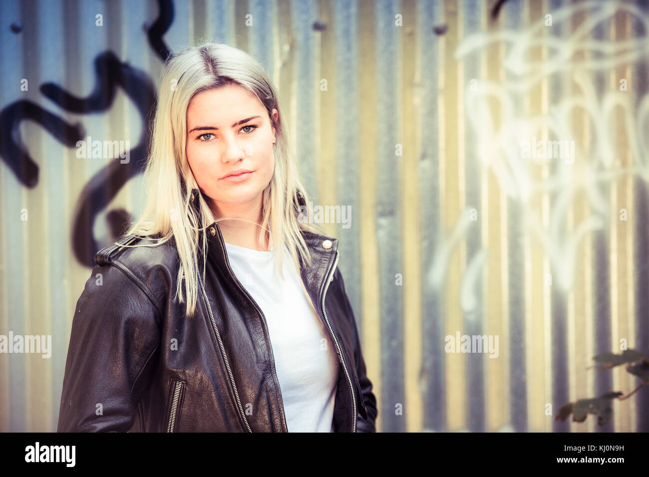 Jugendmädchen Modellierung in Großbritannien: Eine junge 16-jährige Teenager Modell, das Tragen eines schwarzen Leder Jacke, Moody, vor einem Graffiti posing abgedeckt Wellblech metall Wand, Großbritannien Stockfoto