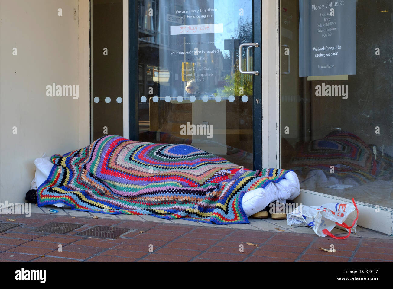 Junger Mann schläft durch den Tag verpackt mit einer Decke geschützt in einem leeren Shop Eingang in einem Einkaufszentrum England Großbritannien Stockfoto