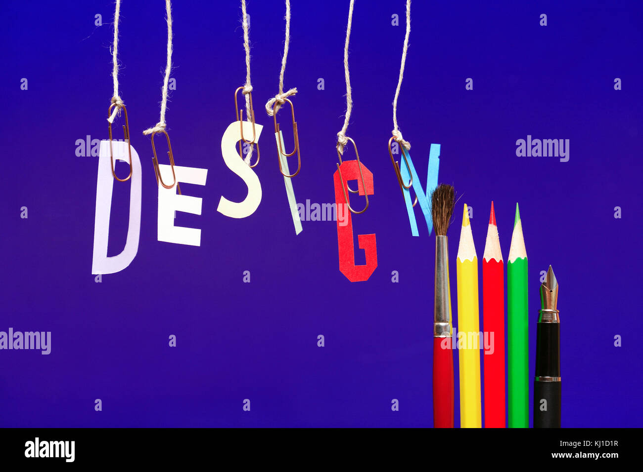 Wort DESIGN aus farbigem Papier Buchstaben hängen mit Seilen in der Nähe von Bleistiften auf blauem Hintergrund Stockfoto