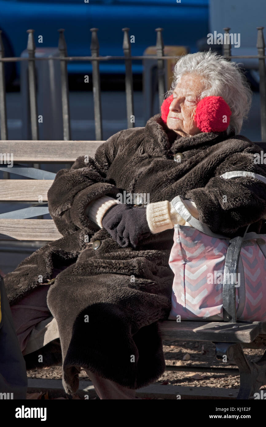 Ein älterer Bürger, die sich in einem schweren Mantel sonnen an einem Wintertag in Vater Demo Square in Greenwich Village, Manhattan, New York City Stockfoto