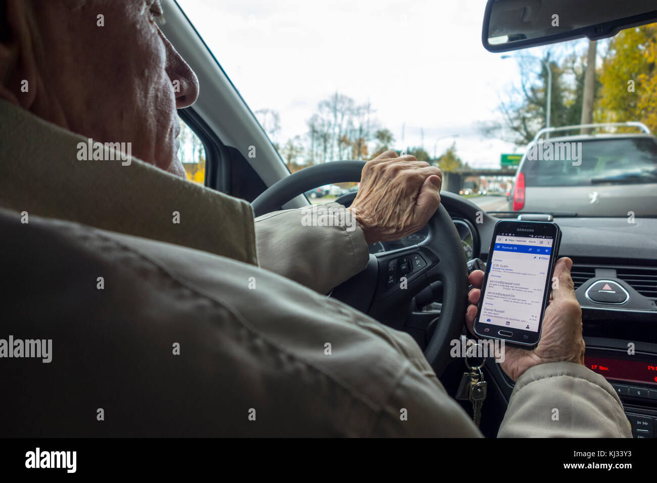 Unverantwortlich älterer Mann am Lenkrad prüfen Nachrichten auf Smart Phone/Smartphone/Handy während der Fahrt Auto auf der Straße Stockfoto