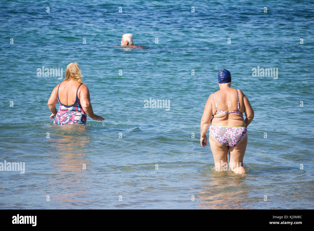 Rückansicht von älteren Frauen, die nach dem täglichen Keep-Fit-Kurs am Strand in Spanien schwimmen gehen Stockfoto
