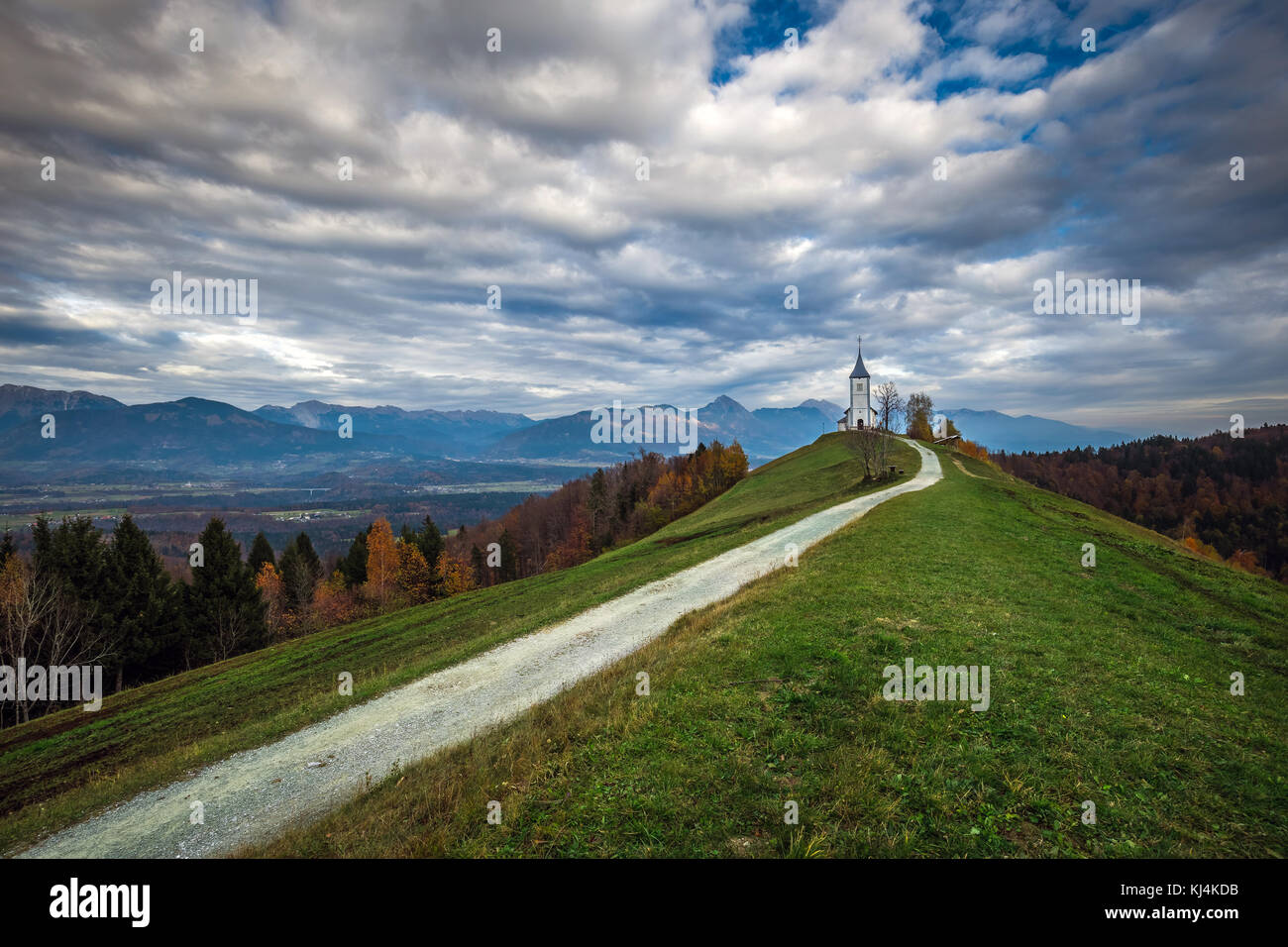 Jamnik, Slowenien - Die schöne Kirche St. Primoz in Slowenien in der Nähe von Jamnik mit wunderschönen Wolken und Julischen Alpen im Hintergrund Stockfoto