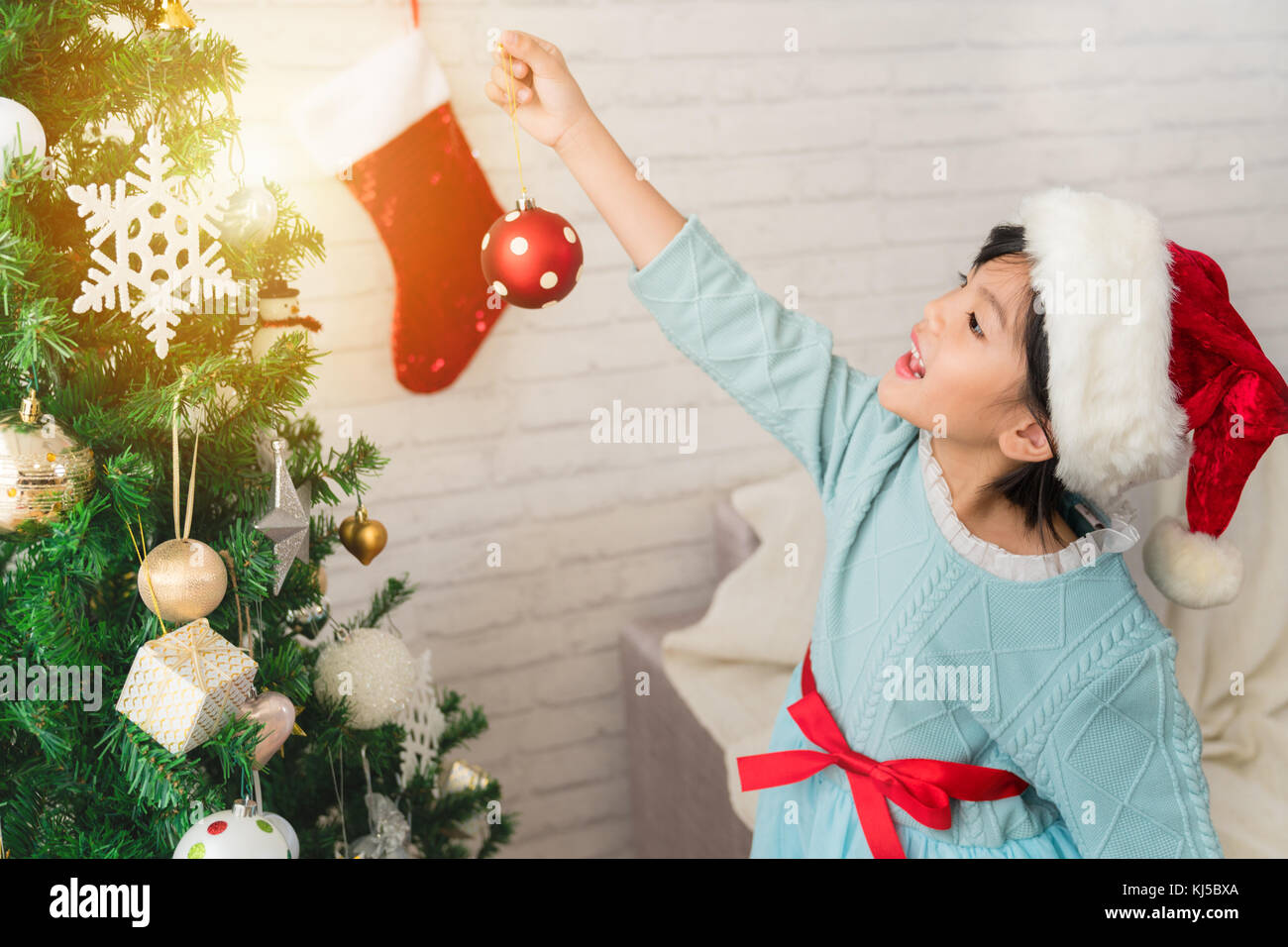 Cute Asian Kind Mädchen schmücken den Weihnachtsbaum im Innenbereich zu Hause am Morgen vor Weihnachten. Portrait Kind schließt sich. Frohe Weihnachten und Stockfoto