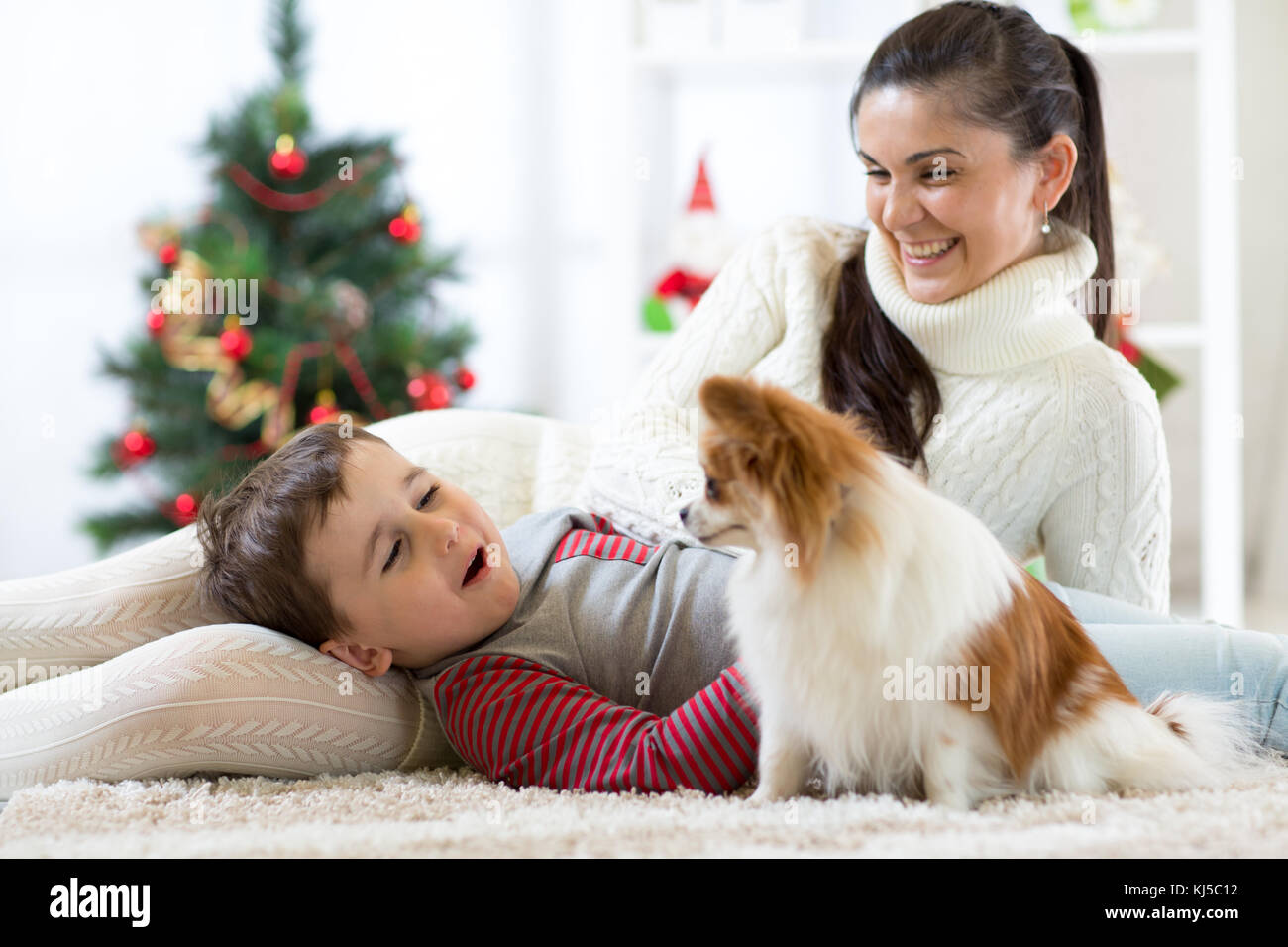 Portrait eines glücklichen Mutter und ihren kleinen Sohn mit Hund verbringen zusammen Weihnachten zu Hause in der Nähe der x-mas Tree Stockfoto