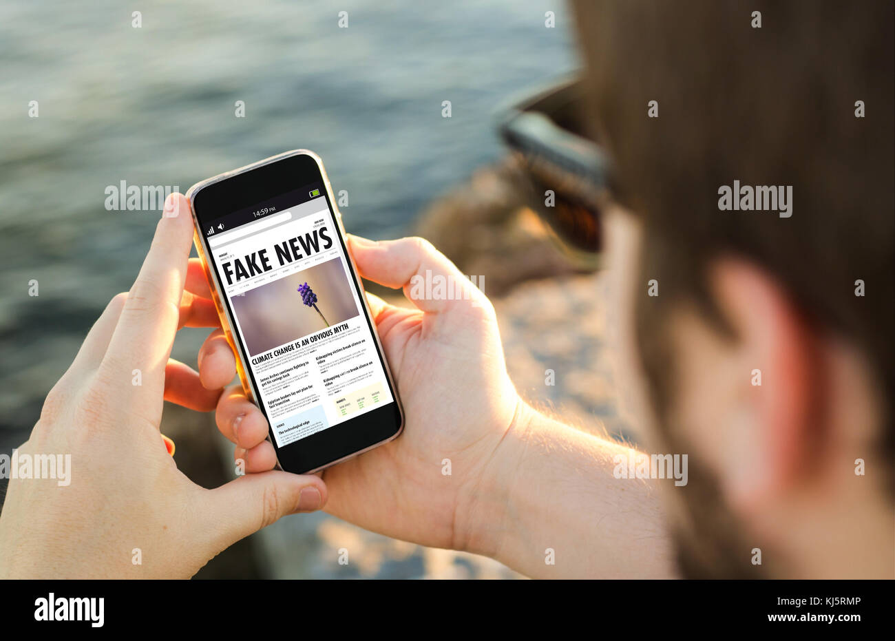 Mann an der Küste, der sein Smartphone benutzt, um gefälschte Nachrichten zu lesen. Alle Bildschirmgrafiken sind zusammengesetzt. Stockfoto