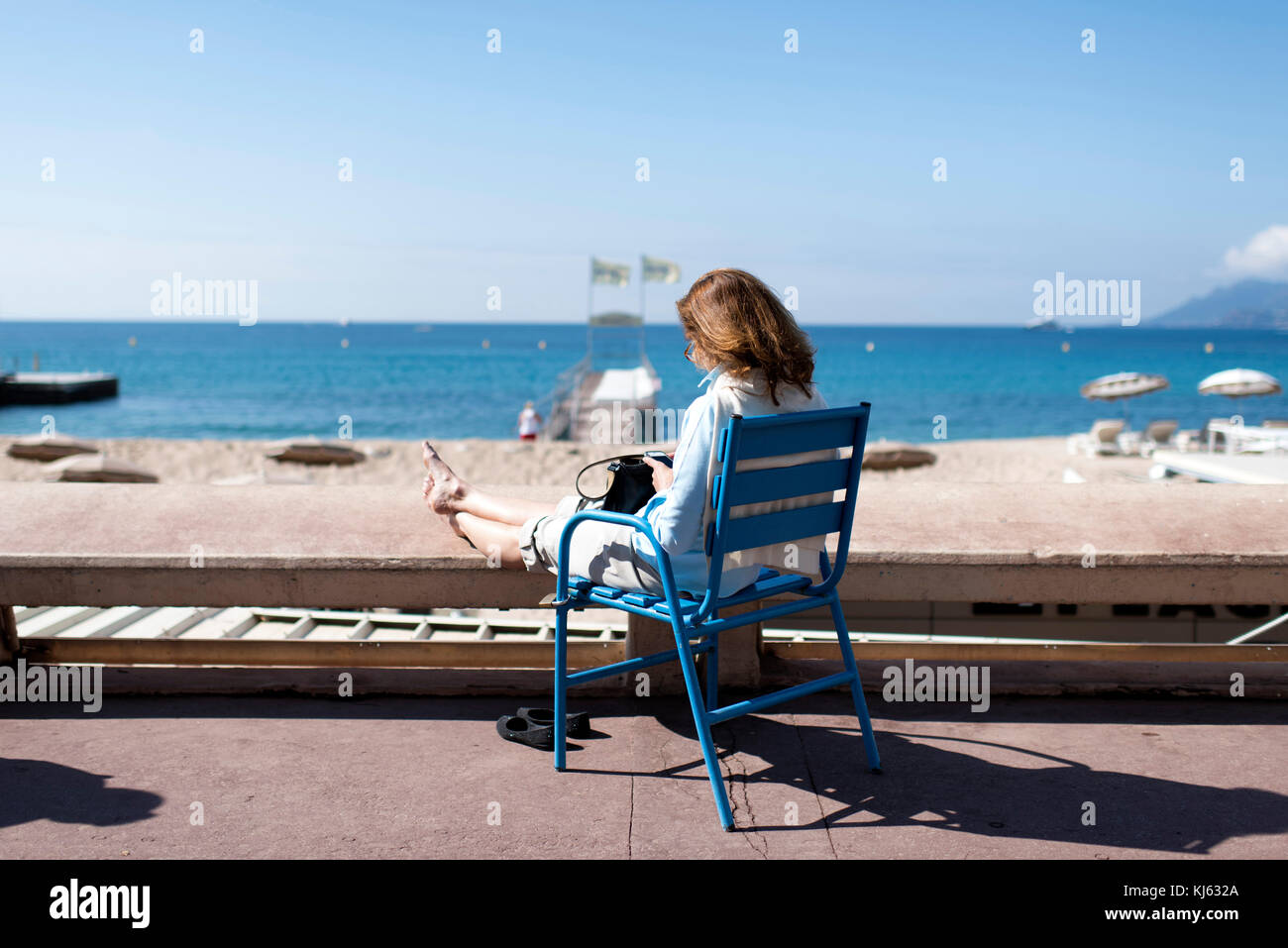 Frau auf Ihrem Smartphone, sitzend, mit Blick auf das Meer, auf dem Boulevard de la Croisette in Cannes. Stockfoto