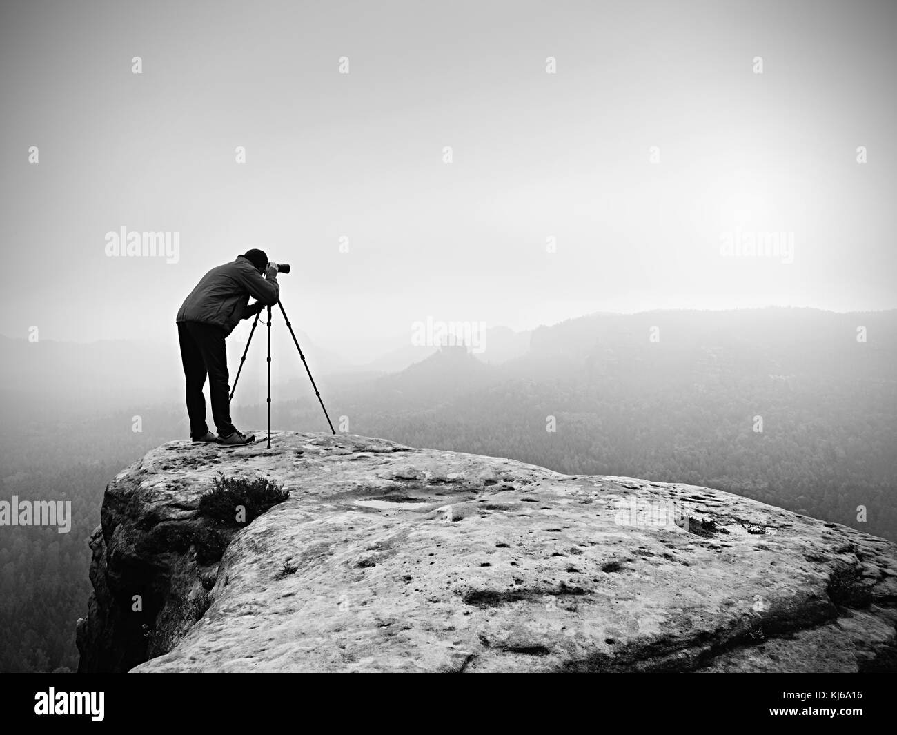 Wanderer mit Kamera auf Stativ nimmt Bild von felsigen Gipfel. Allein Fotograf am Rande Foto nebligen Landschaft, Wald im Tal. Stockfoto