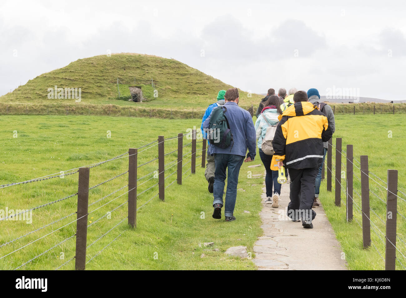 Tour Gruppe und Guide zu Fuß zum geschützten Eingang von Maeshowe Chambered Cairn, Teil des Herzen des neolithischen Orkney-Weltkulturerbes, Stockfoto