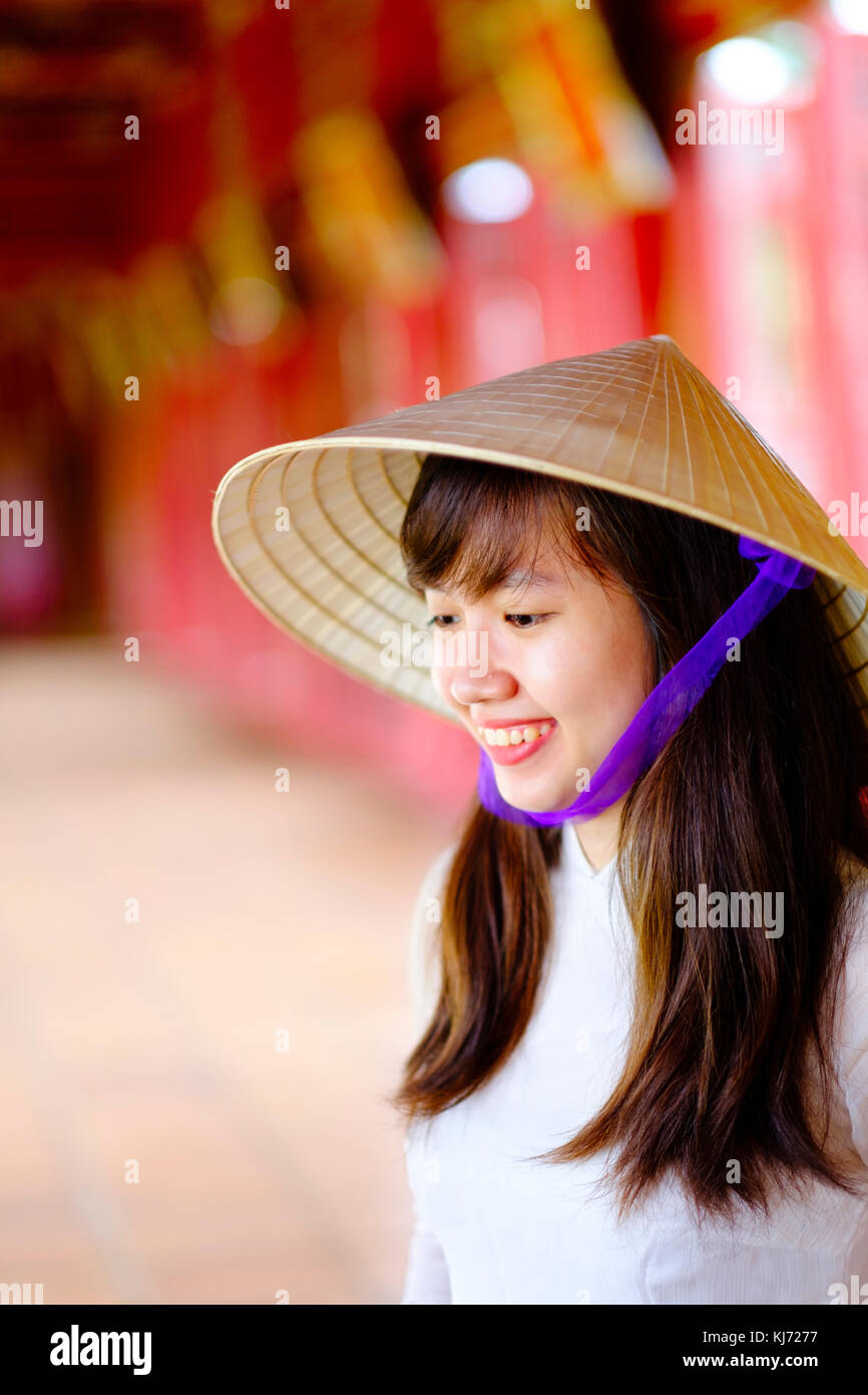 Vietnam, Hue, Forbidden Purple City. Junge Vietnamesin in einem Tempel, die ein traditionelles Ao Dai Kleid und einen nicht-La-asiatischen konischen Hut trägt Stockfoto