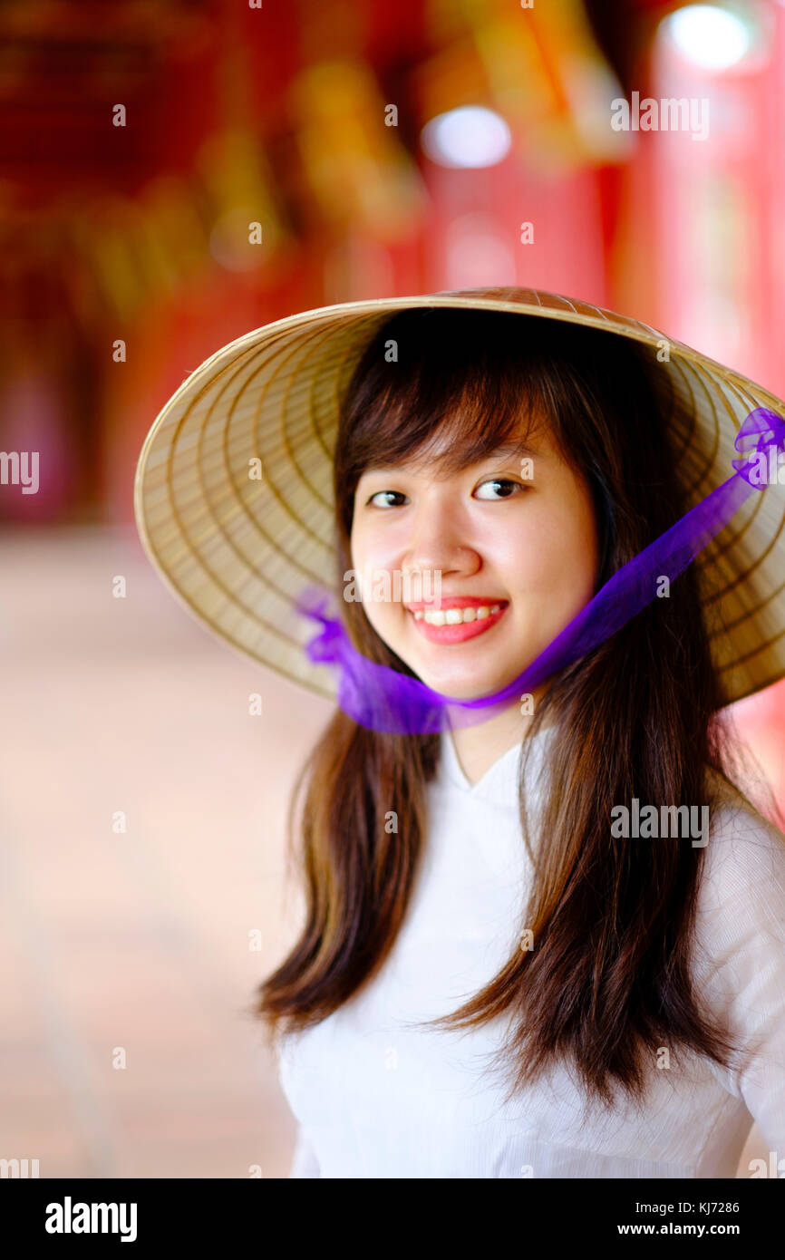 Vietnam, Hue, Forbidden Purple City. Junge Vietnamesin in einem Tempel, die ein traditionelles Ao Dai Kleid und einen nicht-La-asiatischen konischen Hut trägt Stockfoto