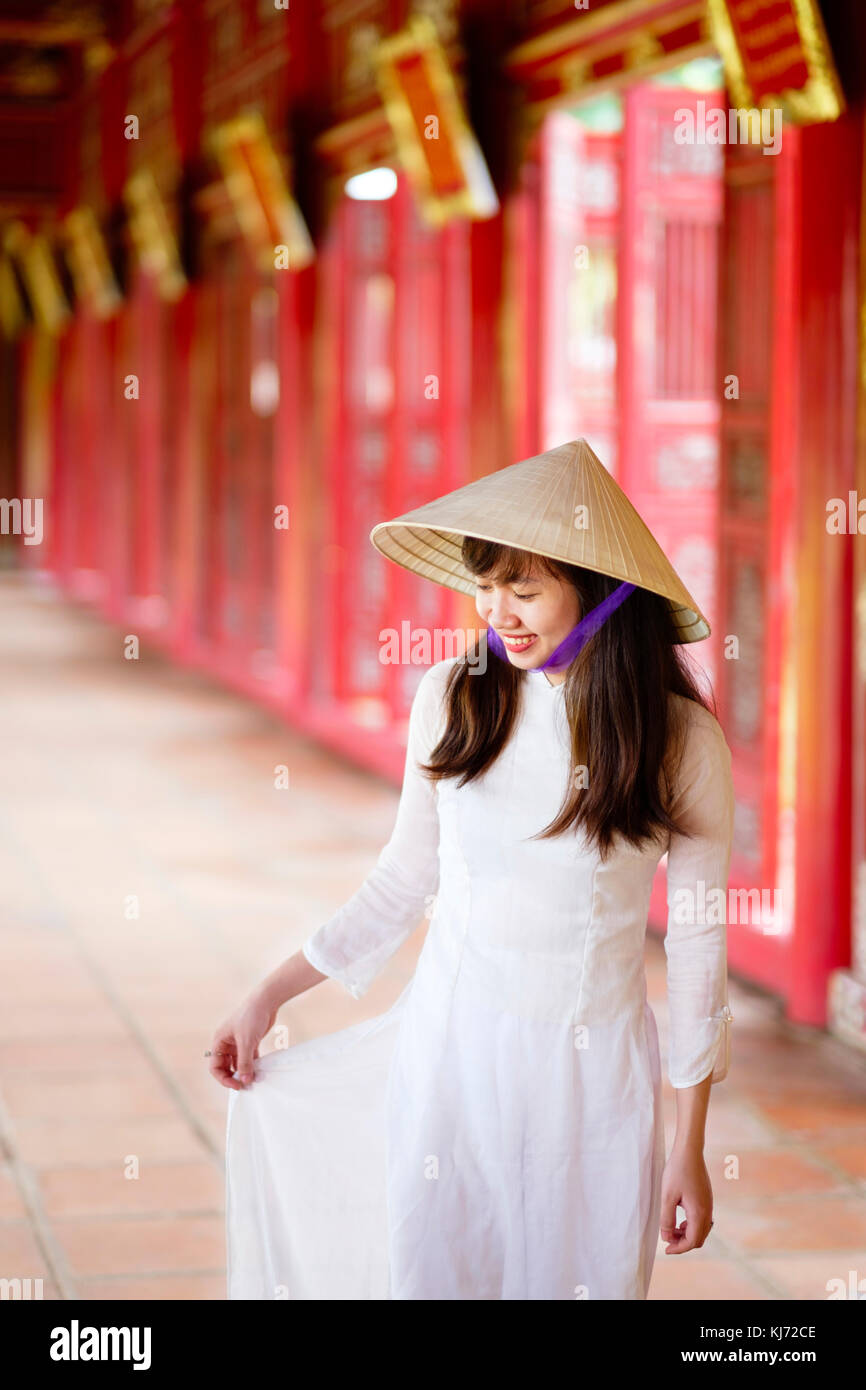 Vietnam, Hue, Forbidden Purple City. Junge Vietnamesin in einem Tempel, die ein traditionelles Ao Dai Kleid und einen nicht-La-asiatischen konischen Hut trägt Stockfoto