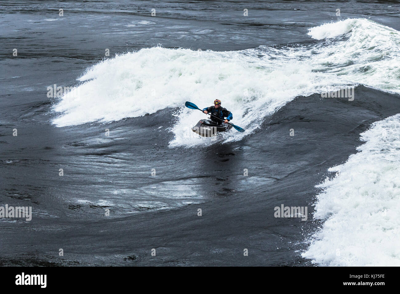 Eine behelmte Mann Kajaks das Gesicht von einer riesigen Welle in Sechelt Rapids, eines der schnellsten Gezeiten der Welt vergeht (Skookumchuck Narrows, British Columbia). Stockfoto
