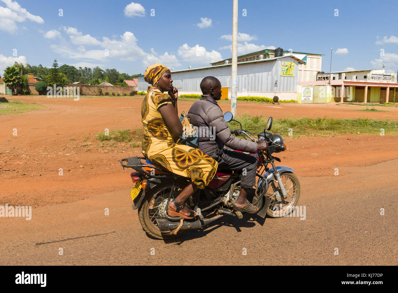 Eine gut gekleidete Frau sitzt auf dem Rücken eines Boda boda Motorrad Taxi, wie sie auf die Straße treibt, Uganda, Ostafrika Stockfoto