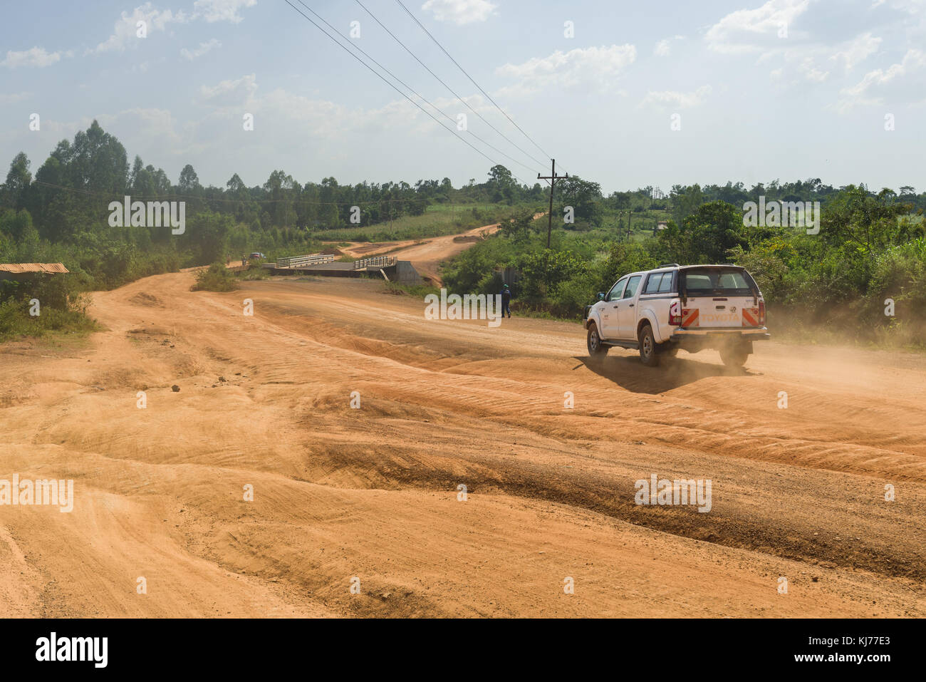Ein 4x4 Fahrzeug fährt nach unten eine unbefestigte Straße im Bau mit Brücke im Hintergrund, Uganda, Ostafrika Stockfoto