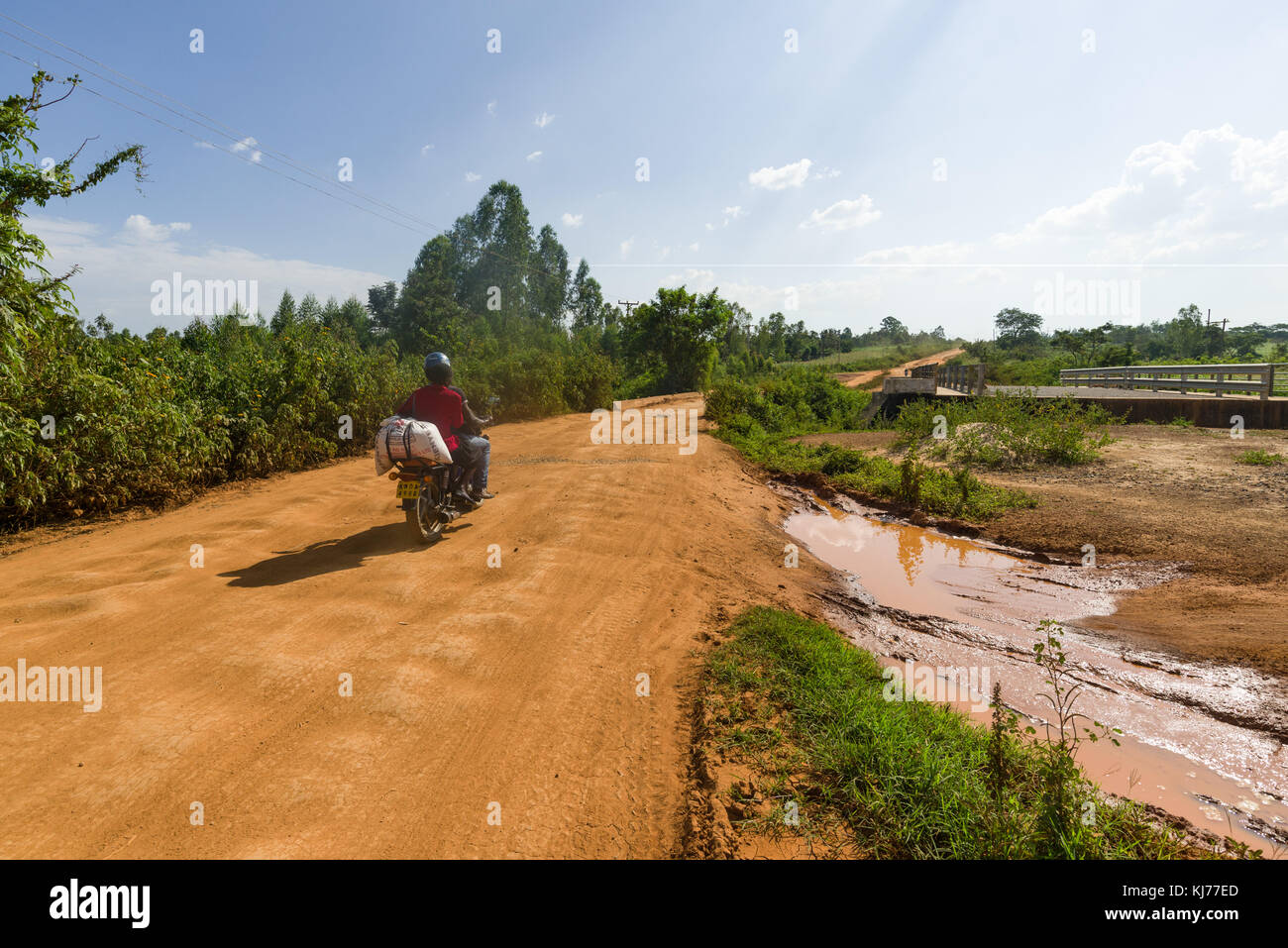 Ein Motorrad boda boda Taxi mit Passagier Antriebe eine teilweise abgeschlossen, unbefestigte Straße mit Brücke im Bau in der Nähe, Kenia, Ostafrika Stockfoto