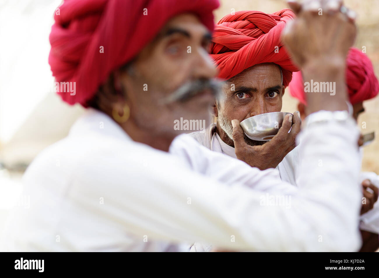 Nahaufnahme eines Rabari Mann mit roten Turban das Trinken aus einer silbernen Schale, andere Männer sind verschwommen. Rajasthan, Indien. Stockfoto