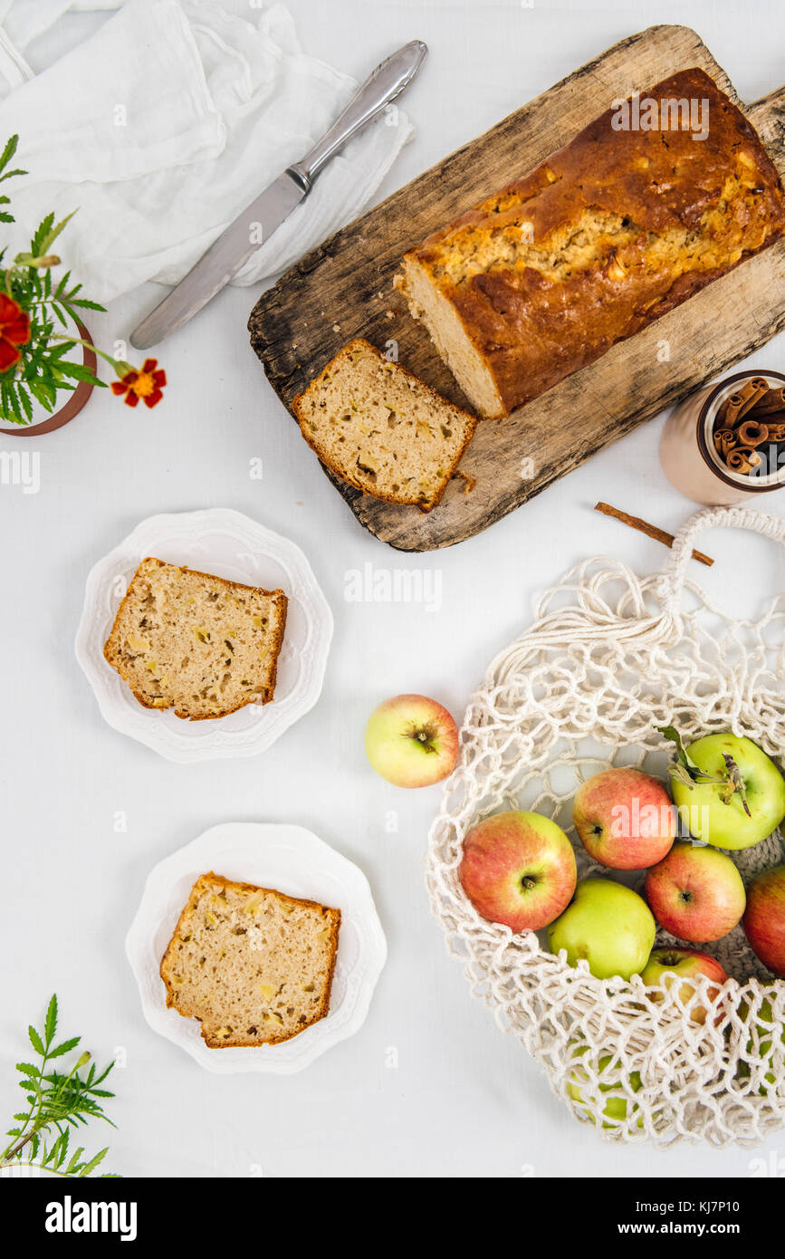 Cinnamon Apple Brot in Scheiben geschnitten auf einer hölzernen Schneidebrett aus Sicht von oben fotografiert. Äpfel in einem Netzbeutel und Apple Brotscheiben auf beiden Platten begleiten. Stockfoto