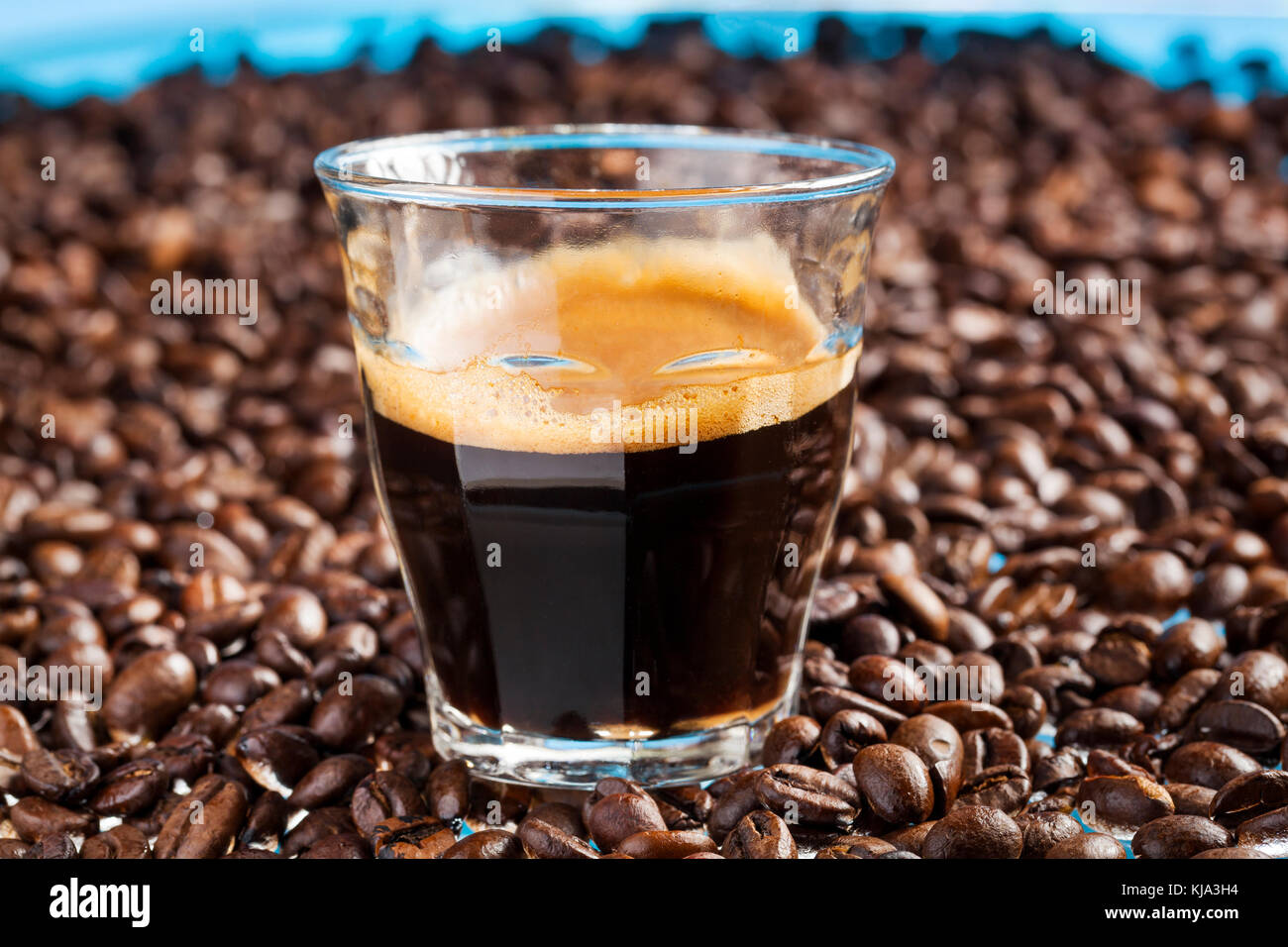 Glas mit doppeltem Espresso, umgeben von Kaffeebohnen Stockfoto