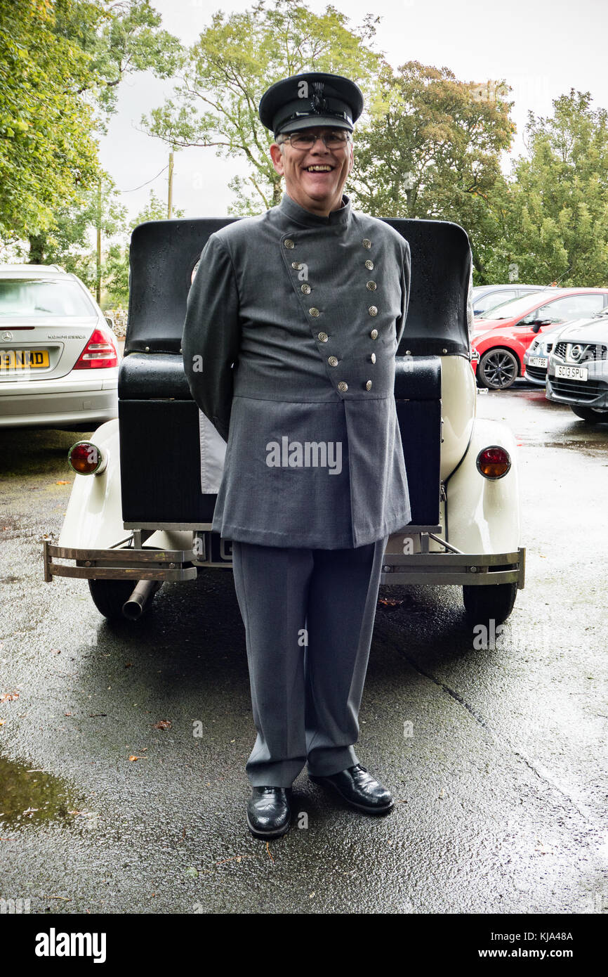 Ein Chauffeur in Uniform vor Faux-Oldtimer Stockfoto