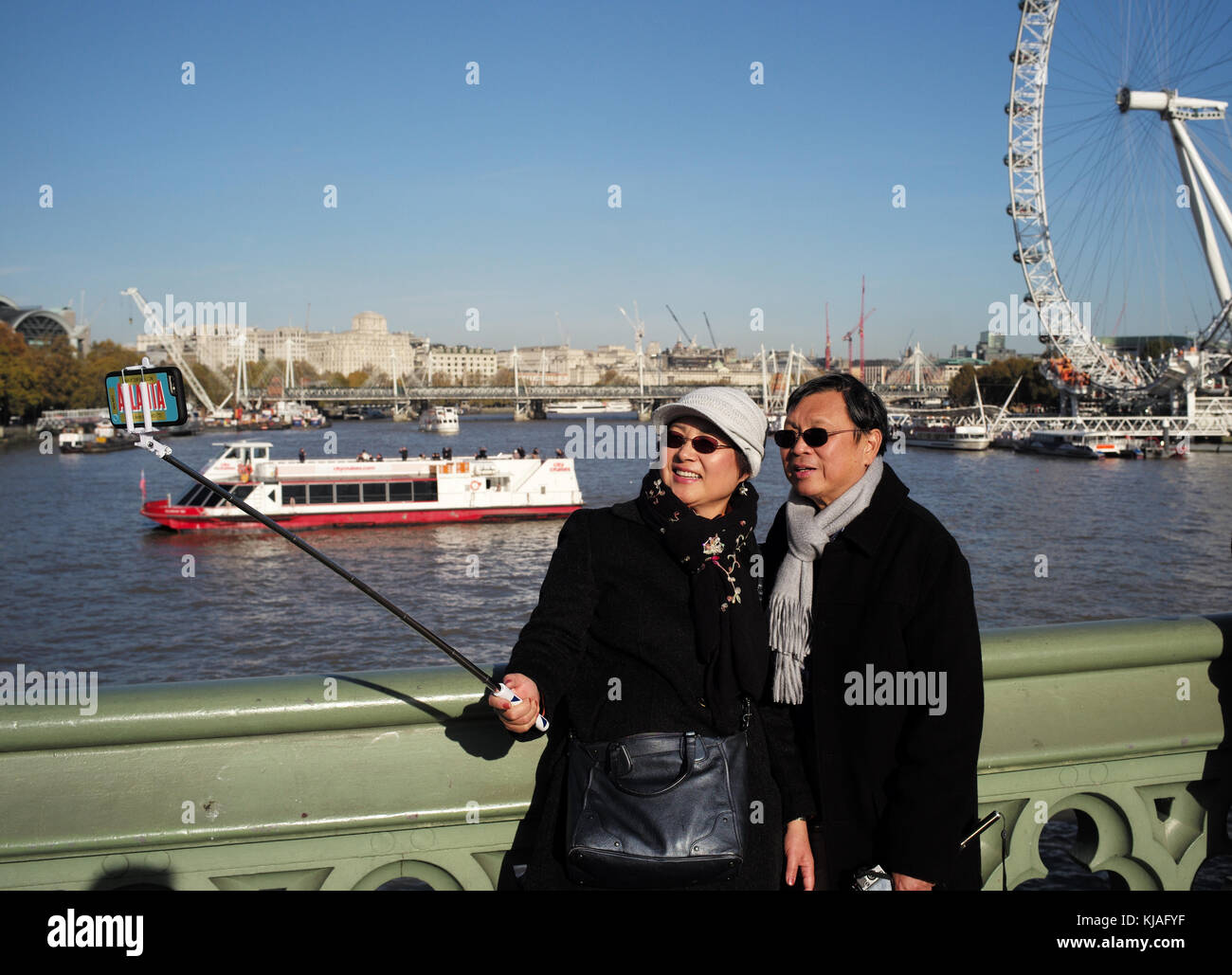 Eine asiatische Paar für einen selfie auf die Westminster Bridge London England mit einem selfie Stick so wie das London Eye in den Hintergrund zu stellen. Stockfoto