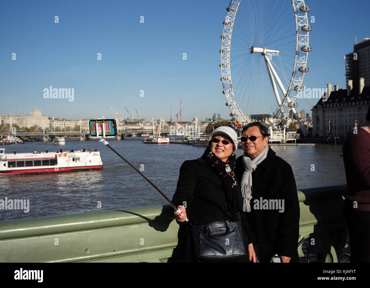 Eine asiatische Paar für einen selfie selfie mit einem Stock auf die Westminster Bridge London mit dem London Eye im Hintergrund darstellen. Stockfoto