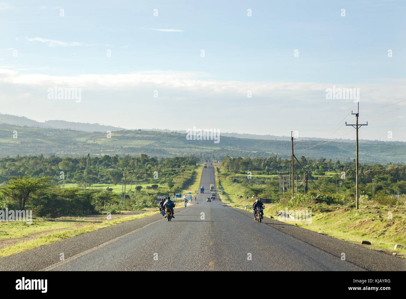 Eine breite, zweispurige Straße durch die Landschaft läuft mit Fahrzeugen und Menschen, Kenia, Ostafrika Stockfoto
