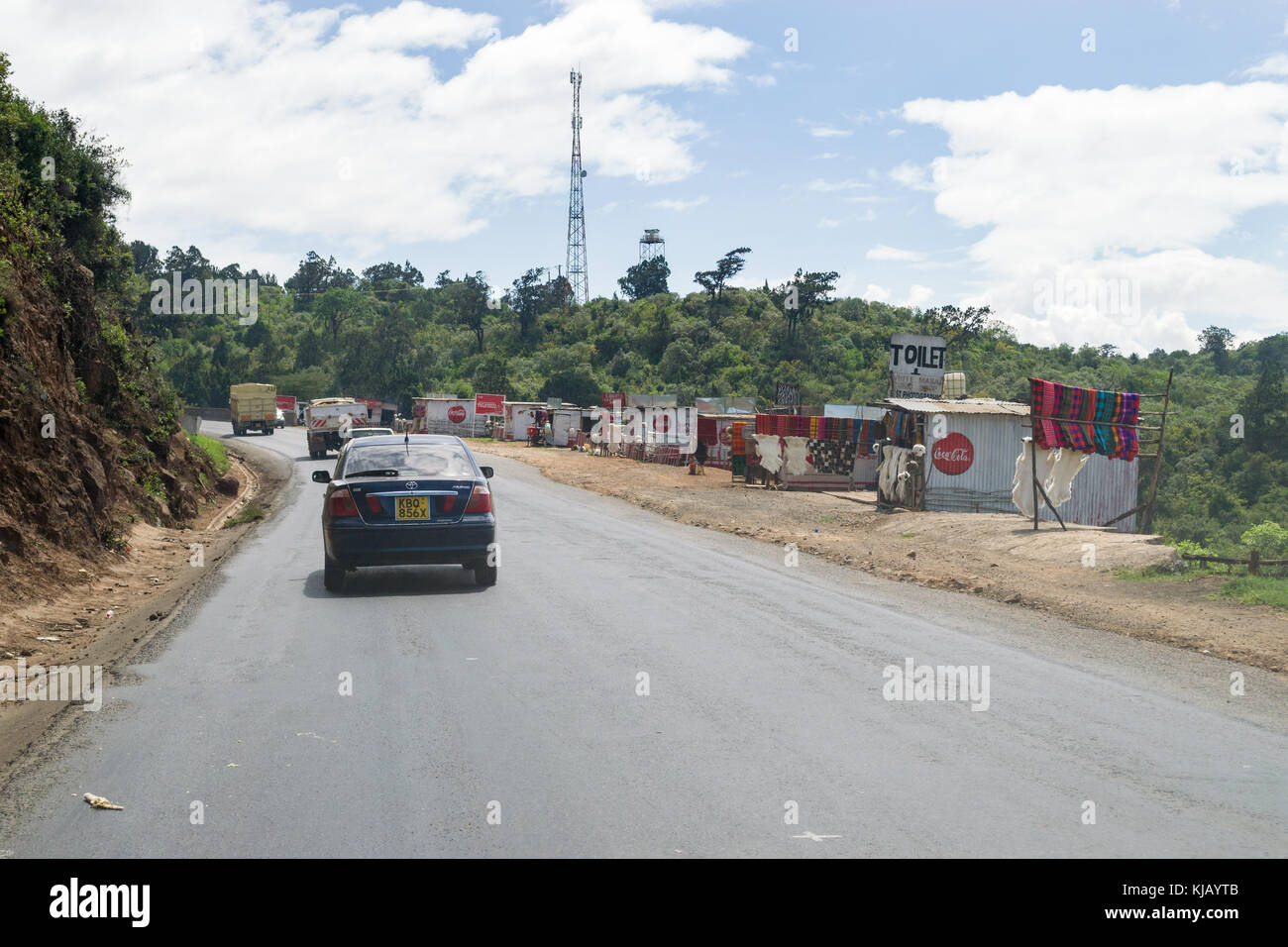 Fahrzeuge fahren auf der Hauptstraße durch das Rift Valley escarpment vorbei an kleinen Metall Hütten am Straßenrand, Kenia, Ostafrika Stockfoto