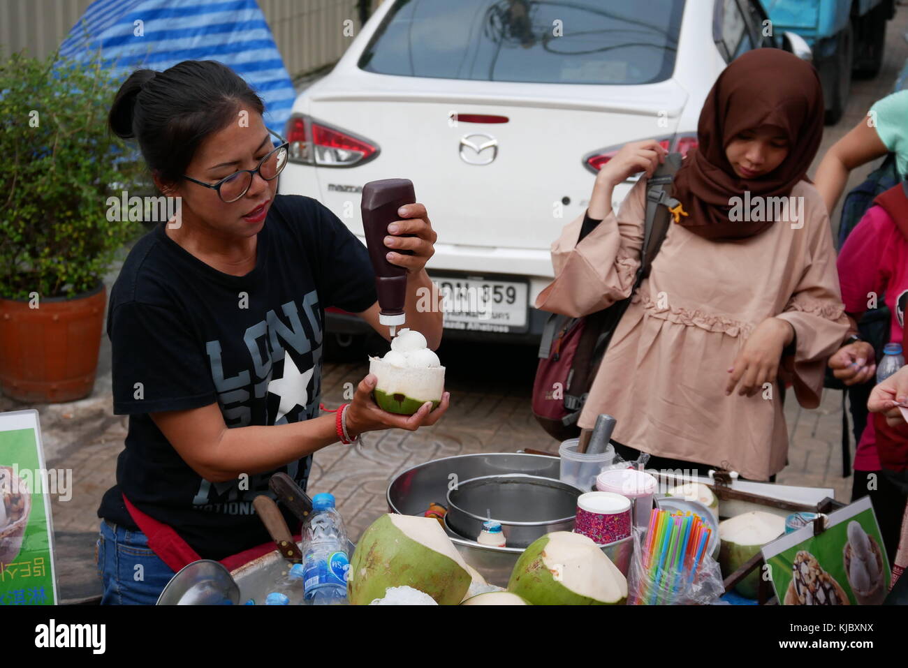 Eine Frau wartet auf ihr Essen bei einem Straßenhändler Kokos-eis in Bangkok, Thailand. Stockfoto